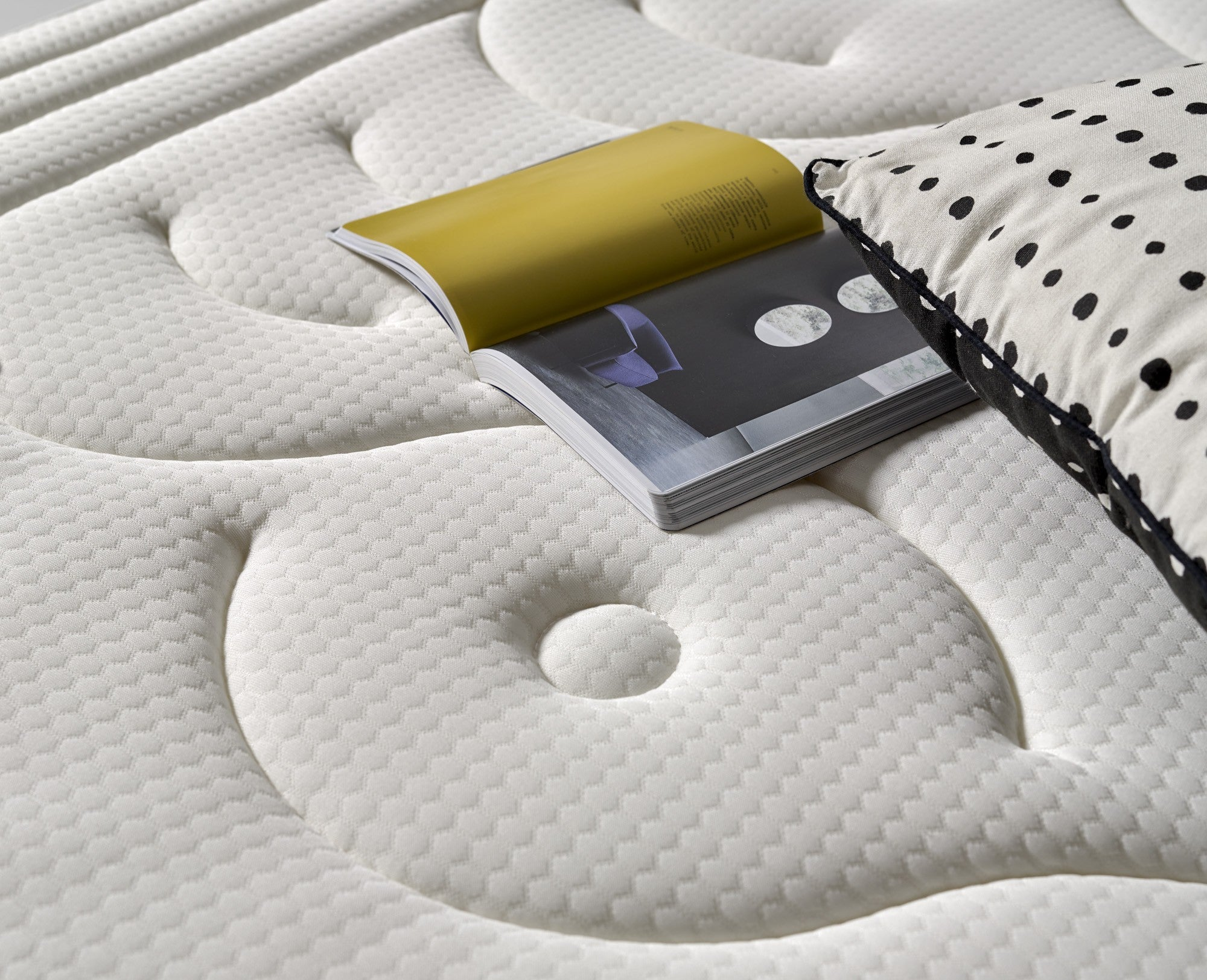 Colchón blanco con libro abierto y almohada con lunares. El colchón tiene una superficie estampada.
