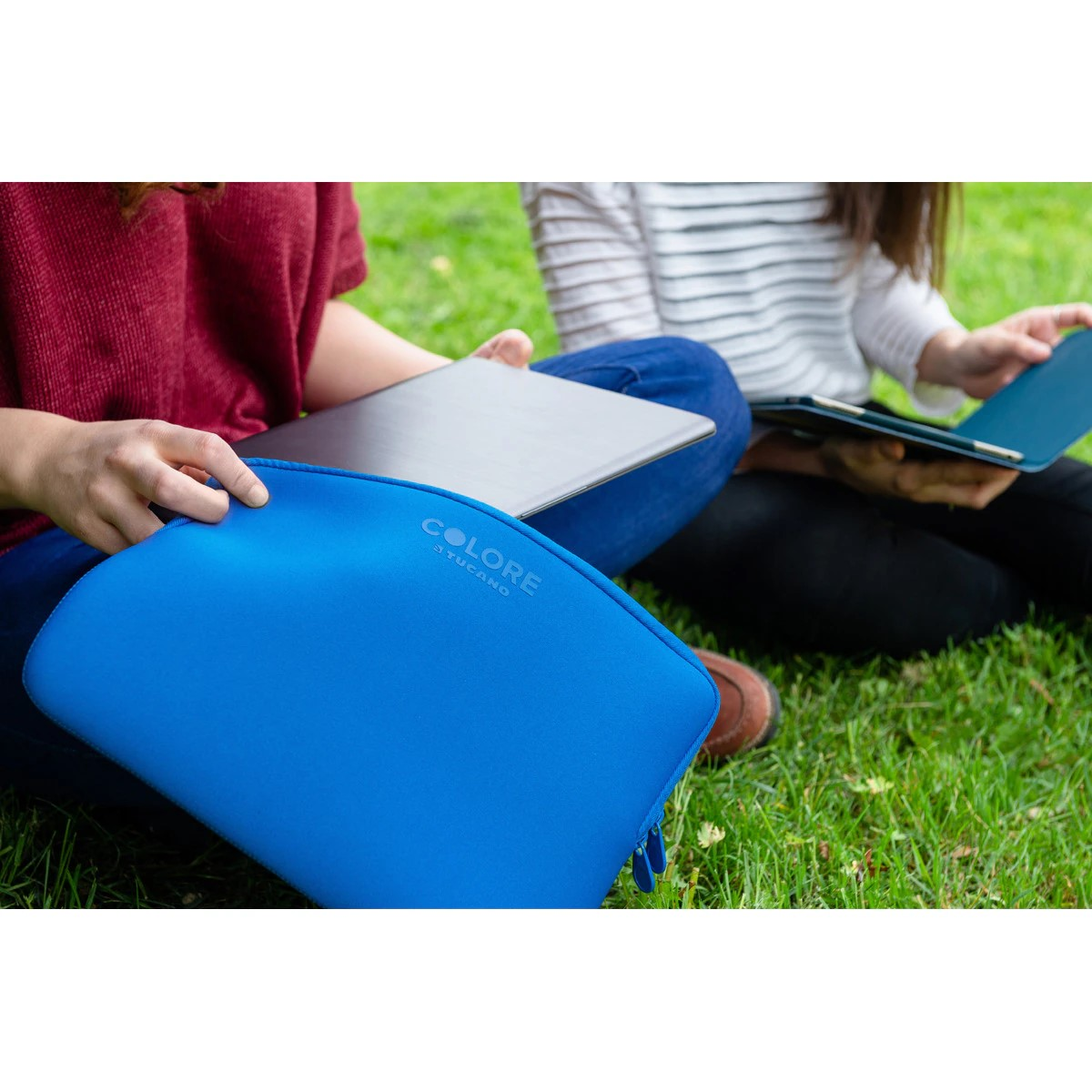 Due persone sull'erba con laptop e una custodia blu. Uno tiene la custodia.