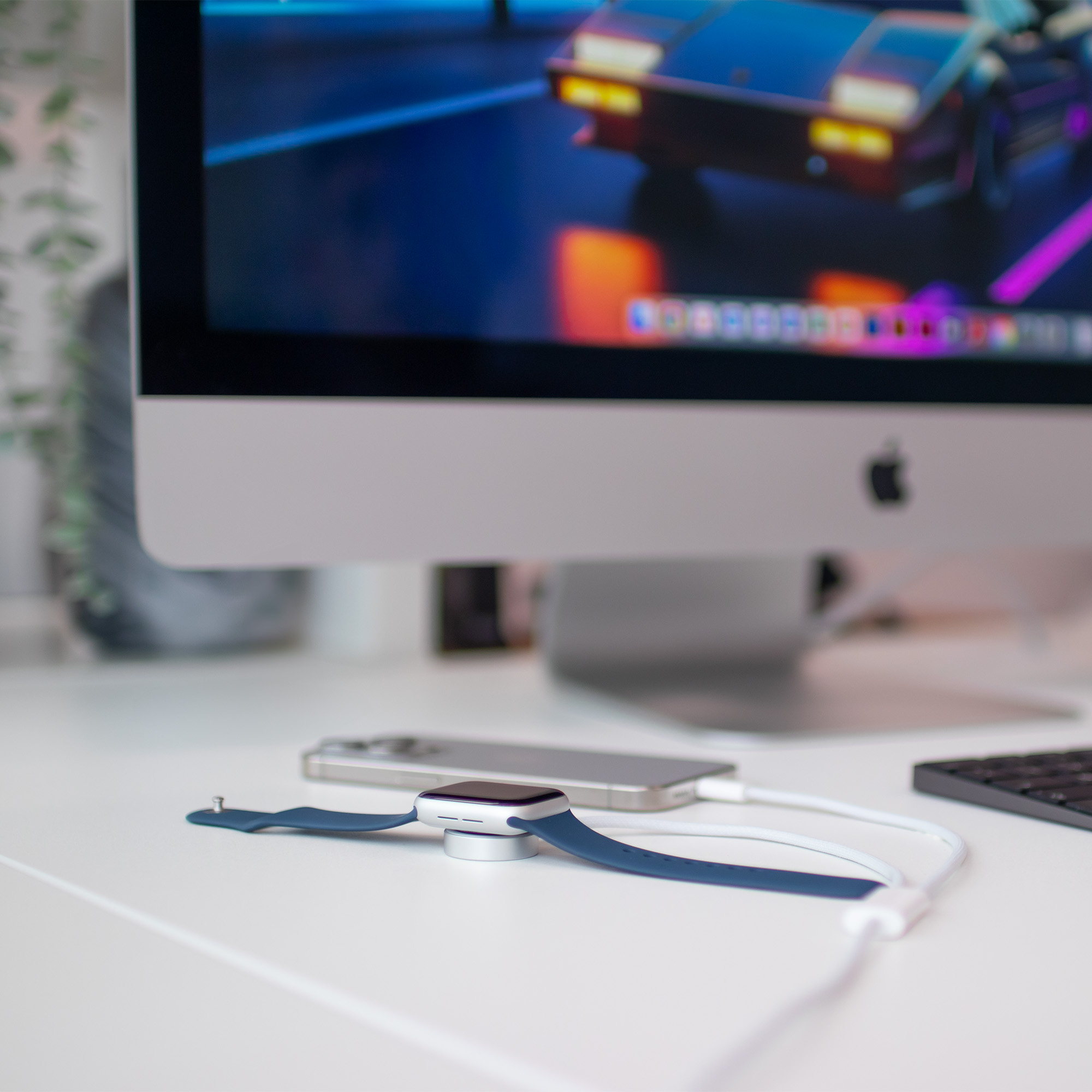 Apple Watch auf Ladegerät, iPhone und Computerbildschirm mit Autobild. Weißer Schreibtisch.