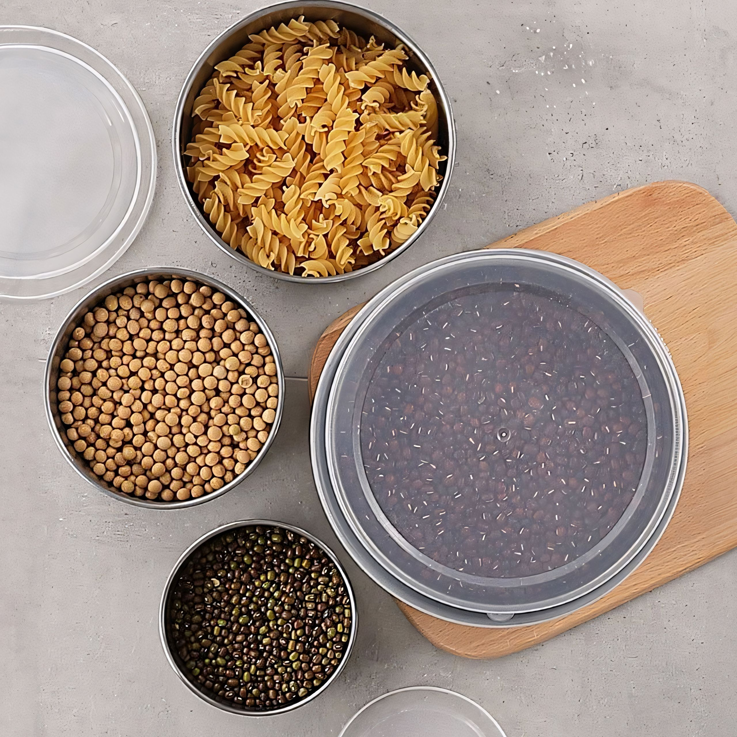 Edelstahlbehälter mit Pasta, Bohnen und Linsen auf grauer Oberfläche.