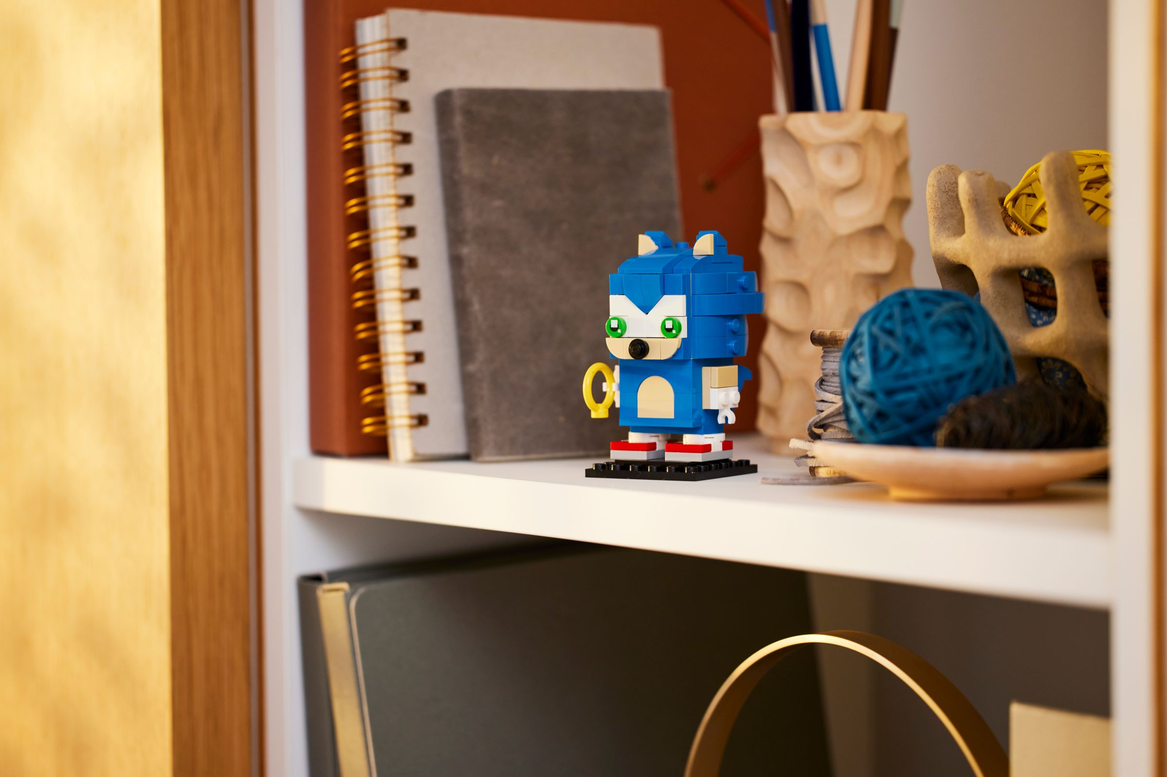 Eine Sonic the Hedgehog Lego-Figur auf einem Regal mit Büchern und dekorativen Gegenständen.
