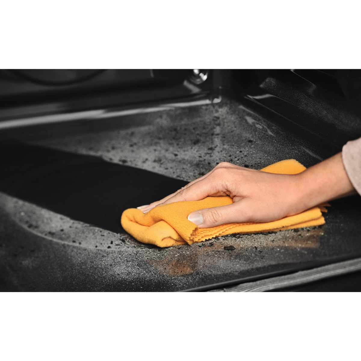 Mano limpiando el interior de un horno con un paño amarillo. Interior oscuro con rastros de suciedad.