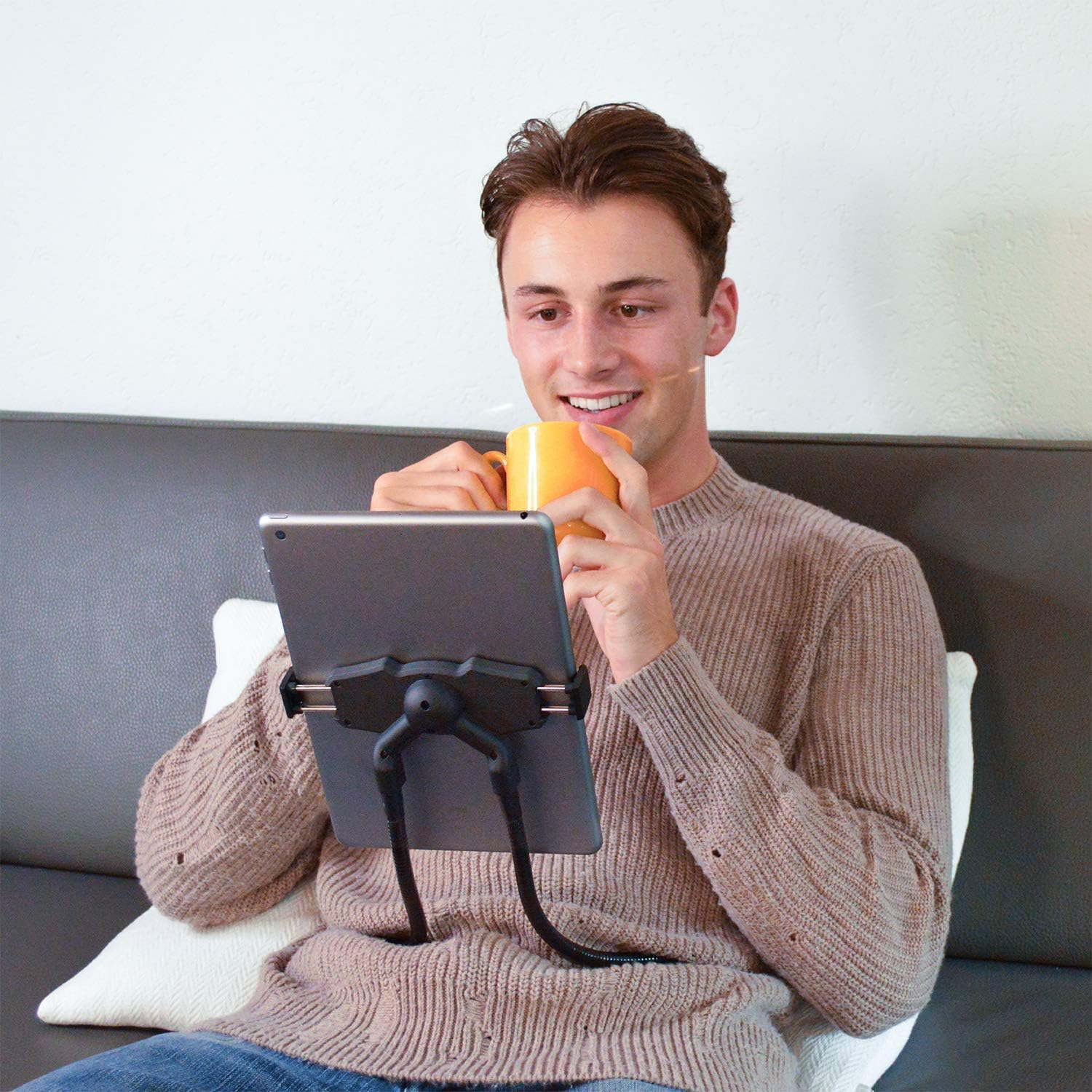 Ein Mann hält einen Becher, während er auf ein Tablet blickt, das auf einem flexiblen Ständer montiert ist.