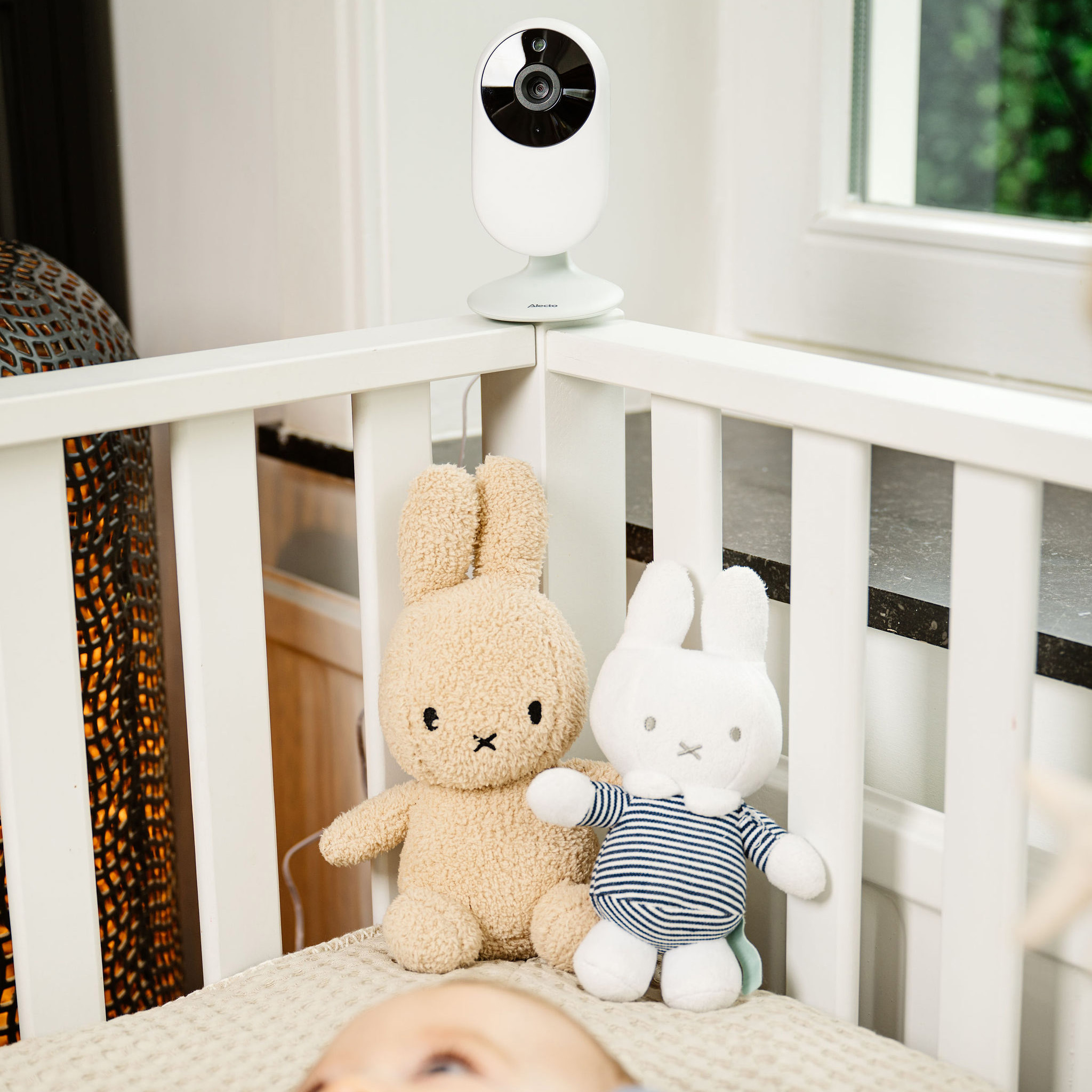Babyphone auf einem Kinderbett mit zwei Stofftieren. Ein Baby liegt im Kinderbett.