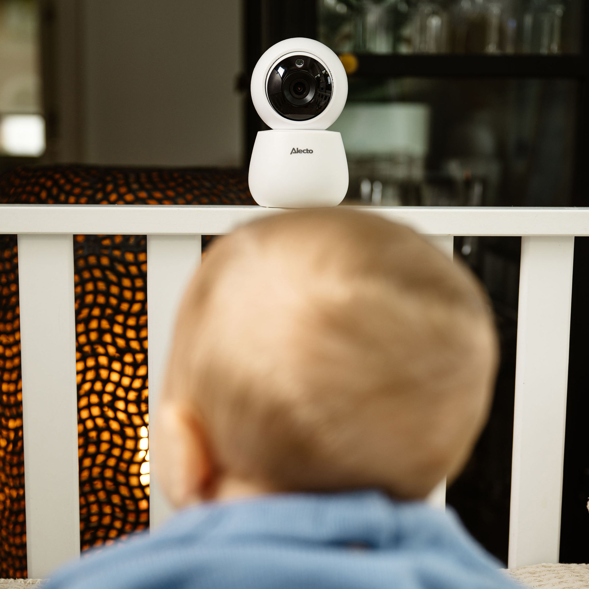 Babyphone-Kamera über einem Kinderbett. Ein Kind im Vordergrund ist unscharf.