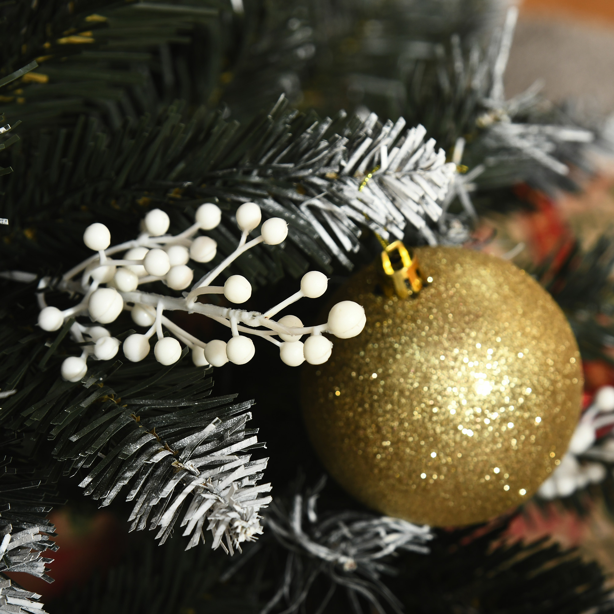Rama de árbol de Navidad con bayas blancas y una bola dorada brillante.