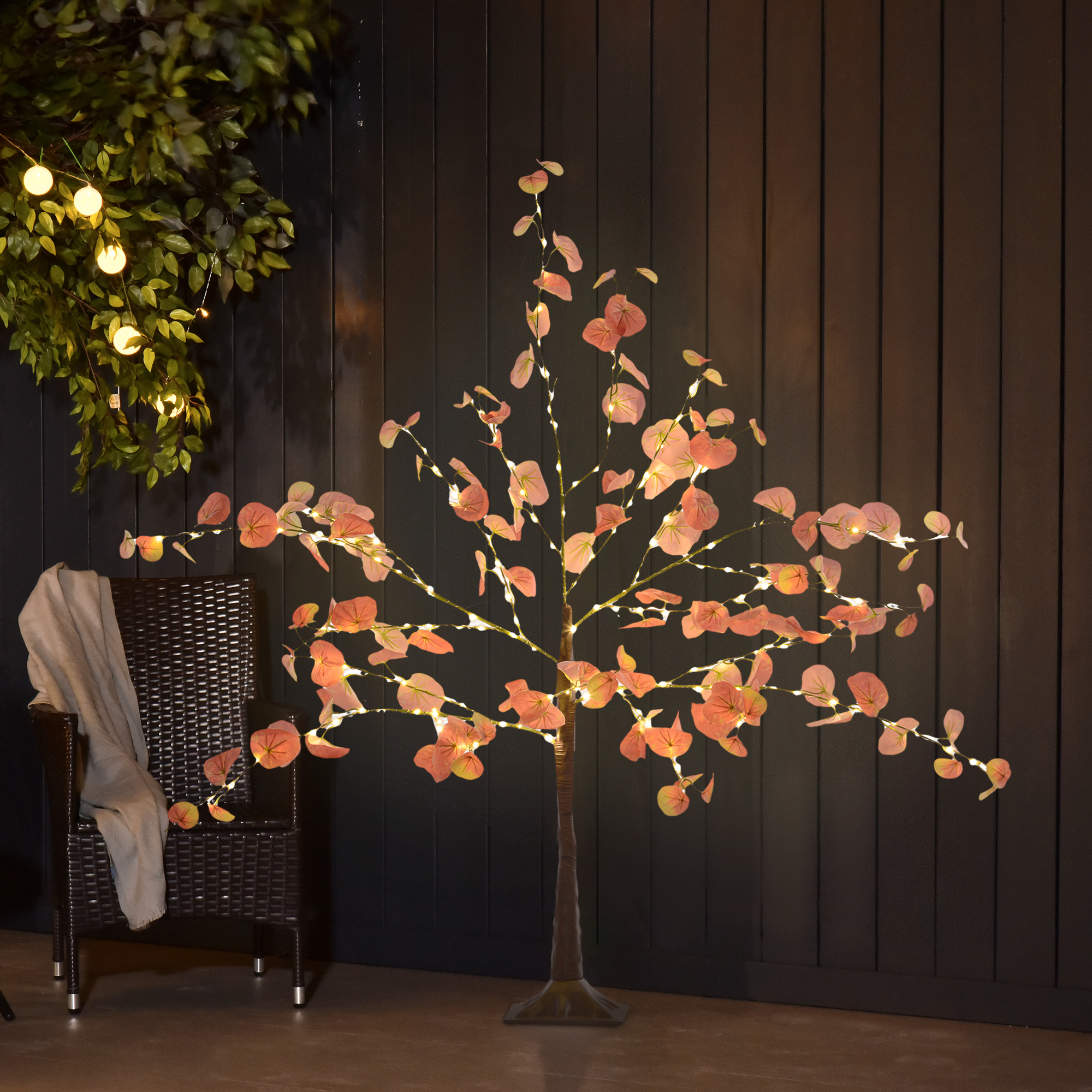 Árbol artificial iluminado con hojas rosas, frente a pared oscura.
