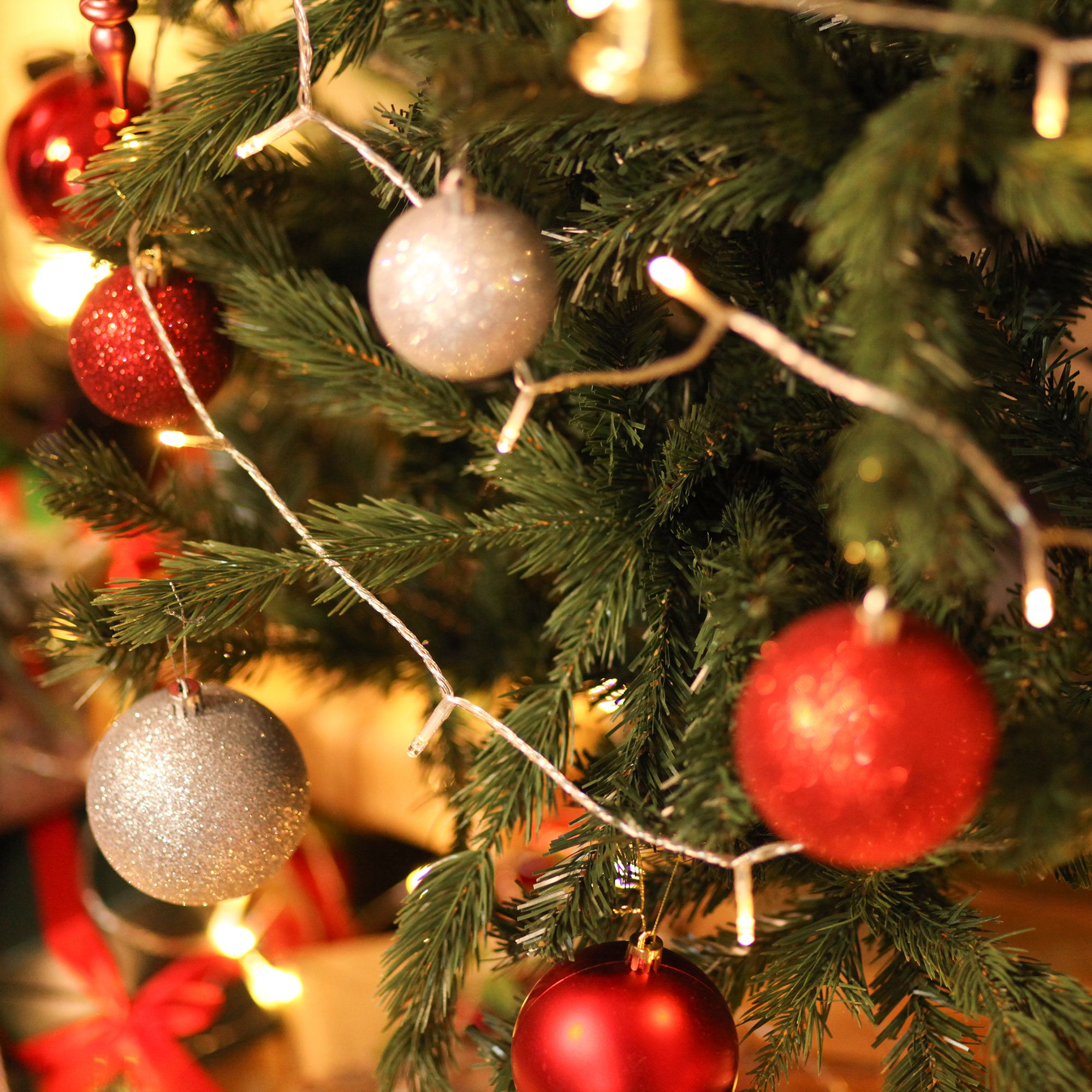 Primer plano de árbol de Navidad con adornos rojos, plateados y blancos y luces blancas.