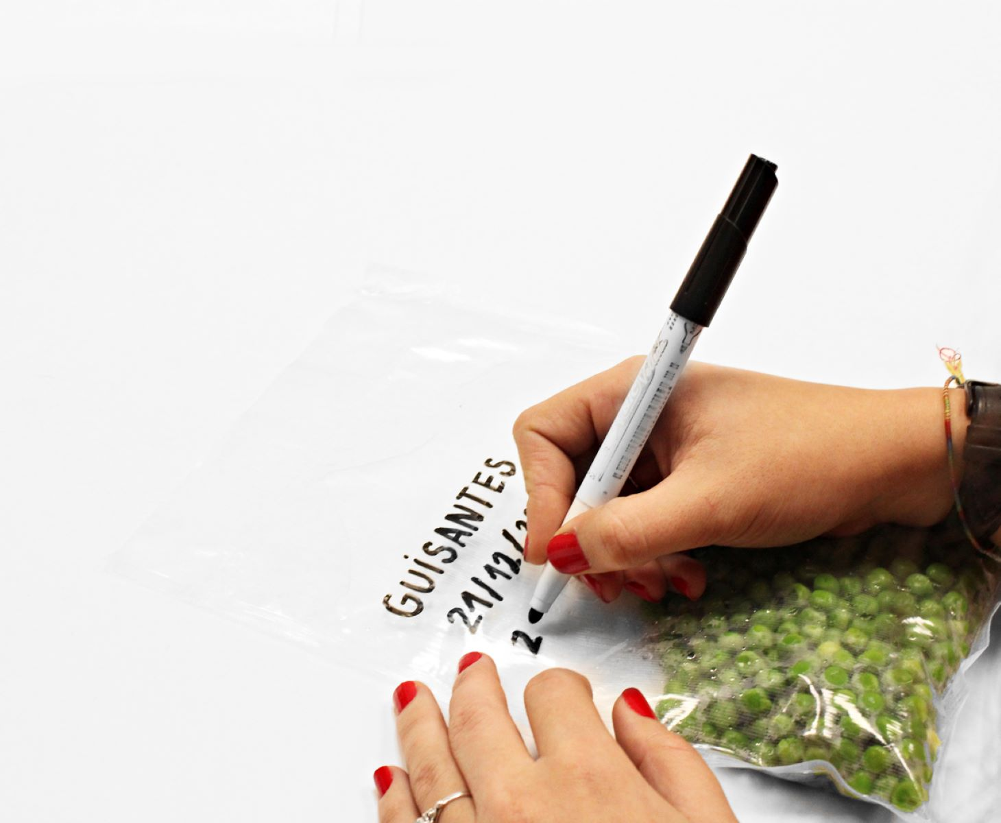 Mano escribiendo 'Guisantes' en una bolsa de guisantes. Esmalte de uñas rojo.