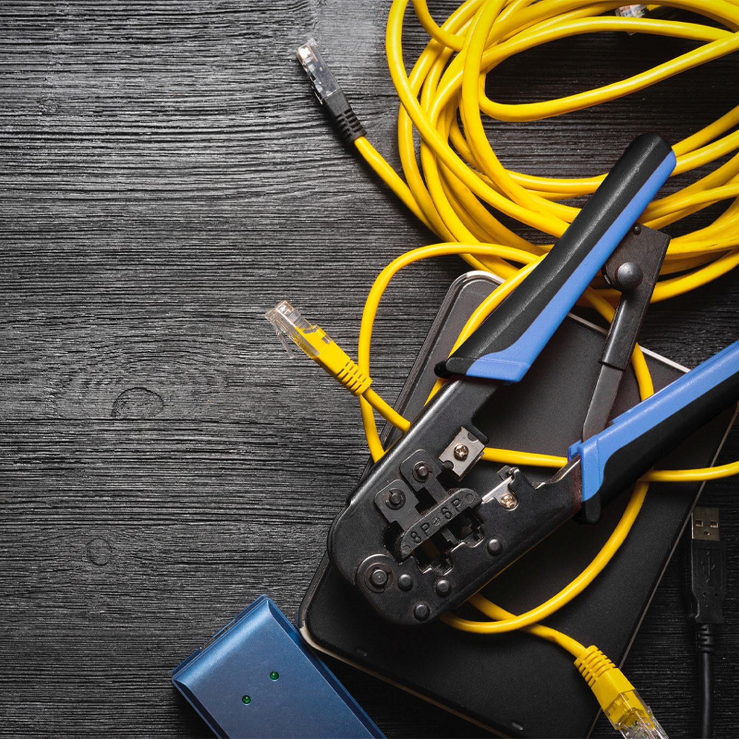 Schwarzer Tisch mit gelbem Kabel, Crimpzange und Netzwerkanschlüssen. Auf dem Tisch liegt ein schwarzes Telefon.