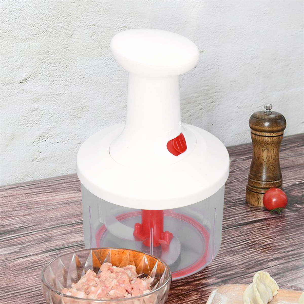 Weißer und roter Zerkleinerer mit Fleisch, einer Tomate und einer Pfeffermühle. Holzoberfläche.