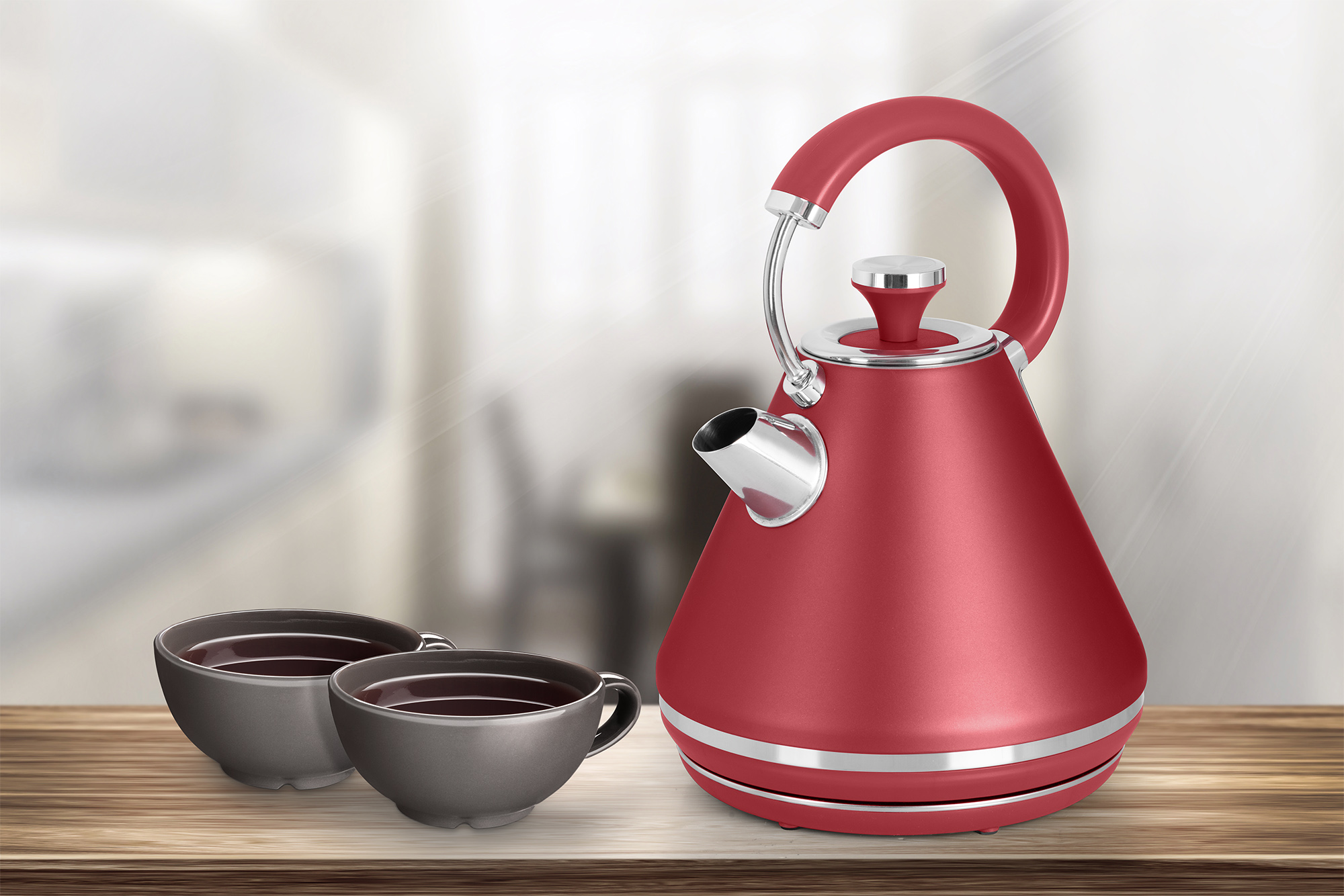 Czerwony czajnik i dwa szare kubki na drewnianym stole z rozmytym tłem.