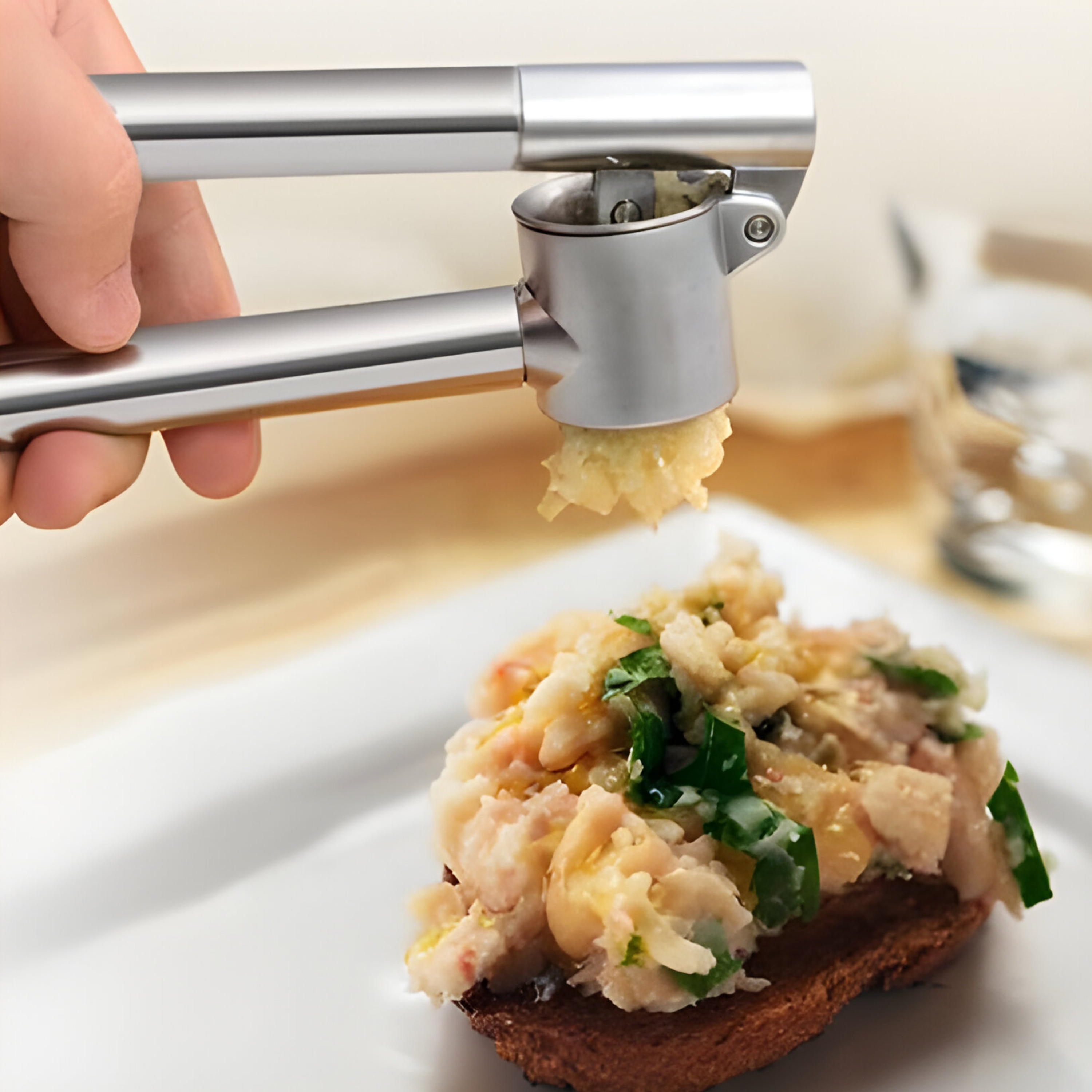 Eine Knoblauchpresse presst Knoblauch auf ein Brotstück mit Belag. Das Brot liegt auf einem weißen Teller.