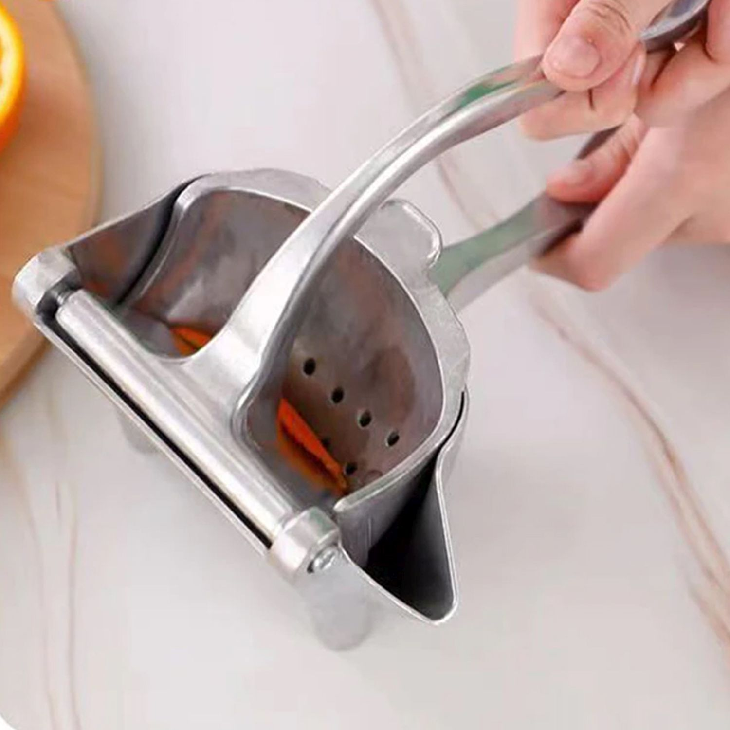 Metall-Zitruspresse mit Orangenscheiben darin. Hand presst den Saft.