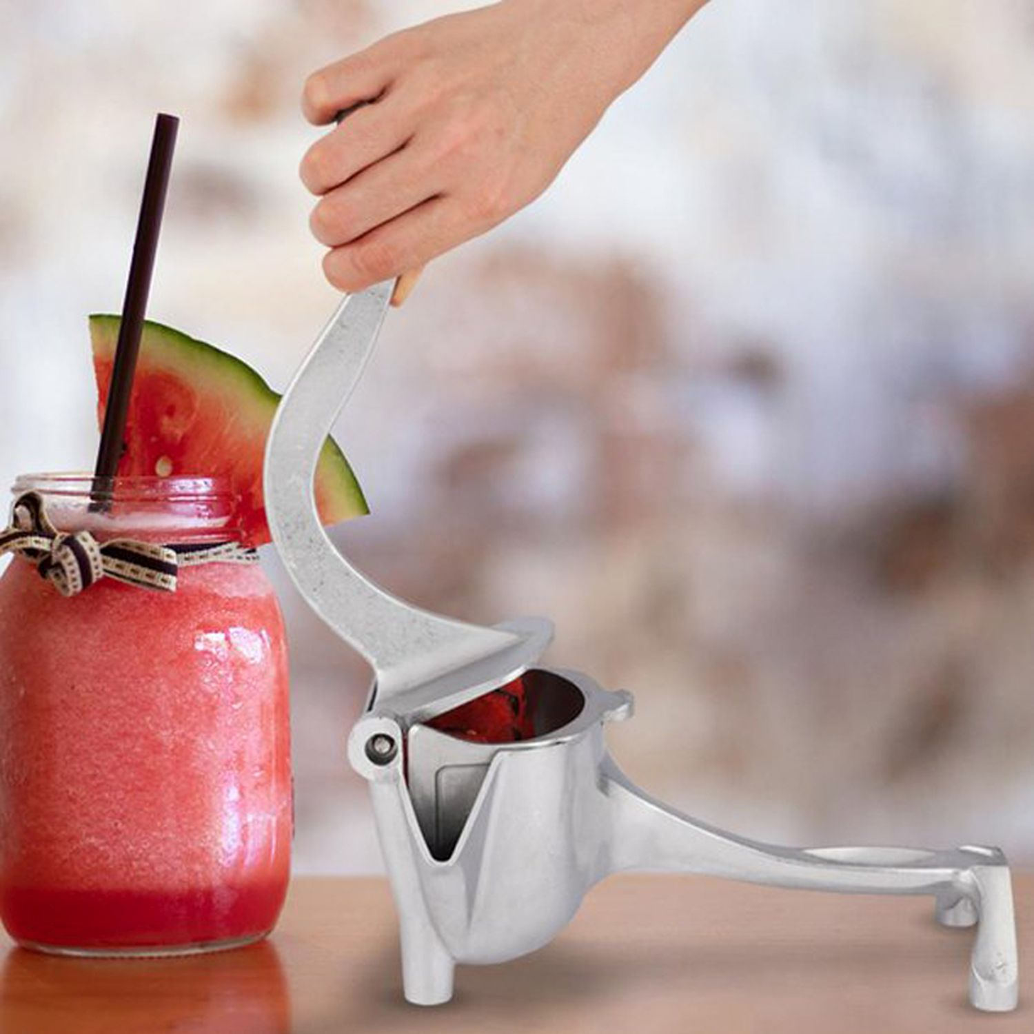 Hand drückt Saftpresse, Glas mit rotem Saft, Strohhalm und Wassermelone.