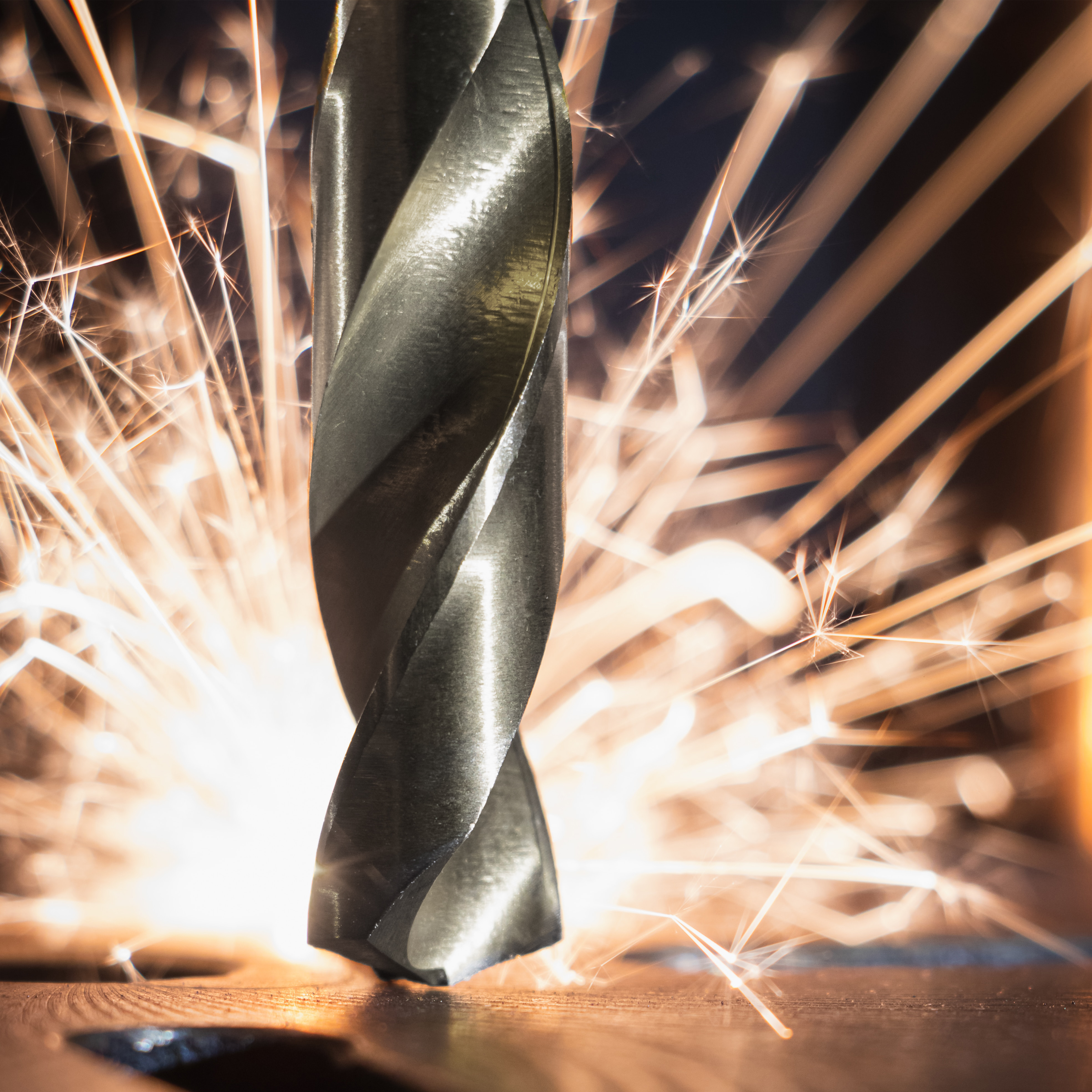 Bohrer mit Funken, Nahaufnahme auf glänzender Metalloberfläche.