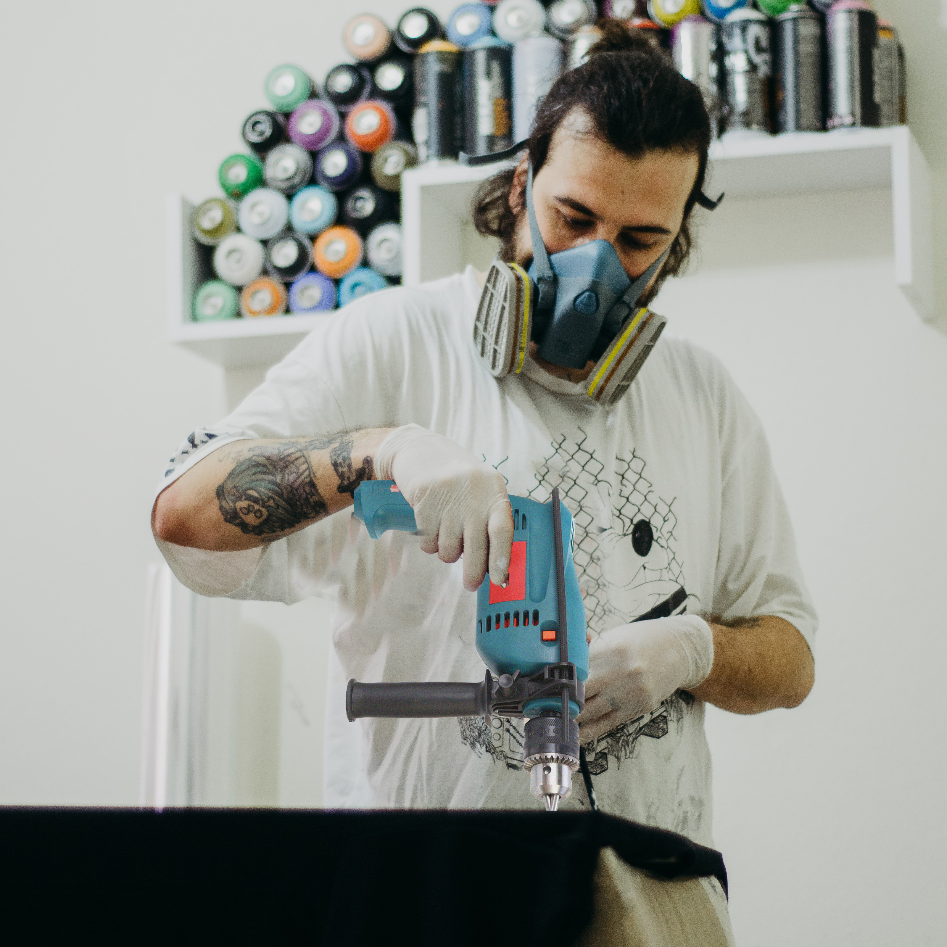 Ein Mann, der eine türkisblaue Bohrmaschine benutzt, trägt Maske und Handschuhe.