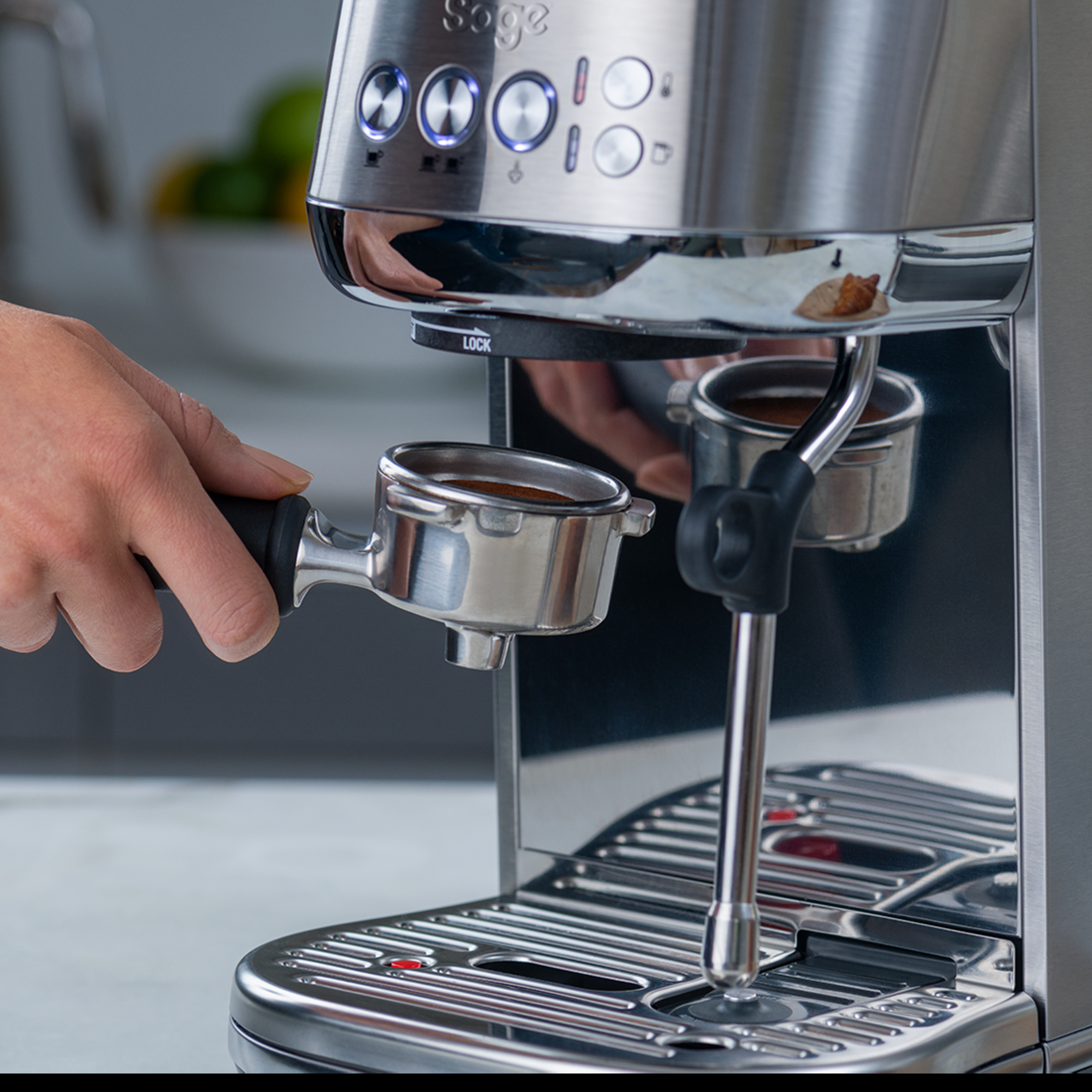 Eine Hand hält einen Siebträger über einer Espressomaschine, Chrom-Finish, Details sichtbar.