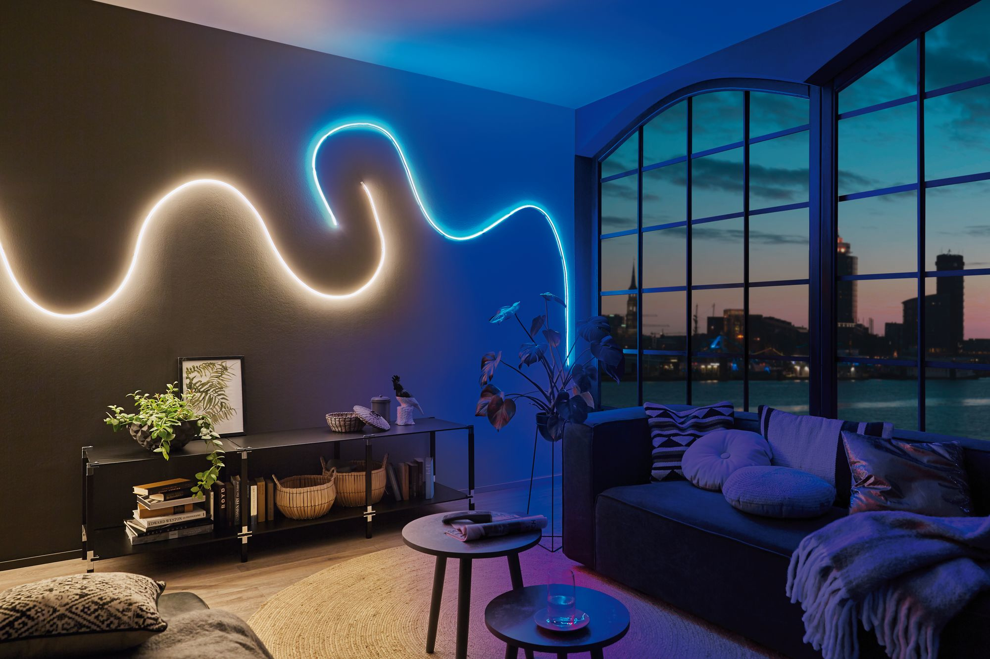 Un salon moderne avec une lumière au néon sur le mur. Un canapé, une table et des plantes sont présents.