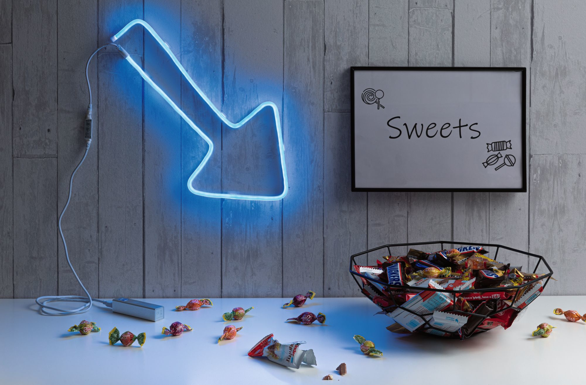 Stół z neonową strzałką, cukierkami i znakiem z napisem „Sweets”.