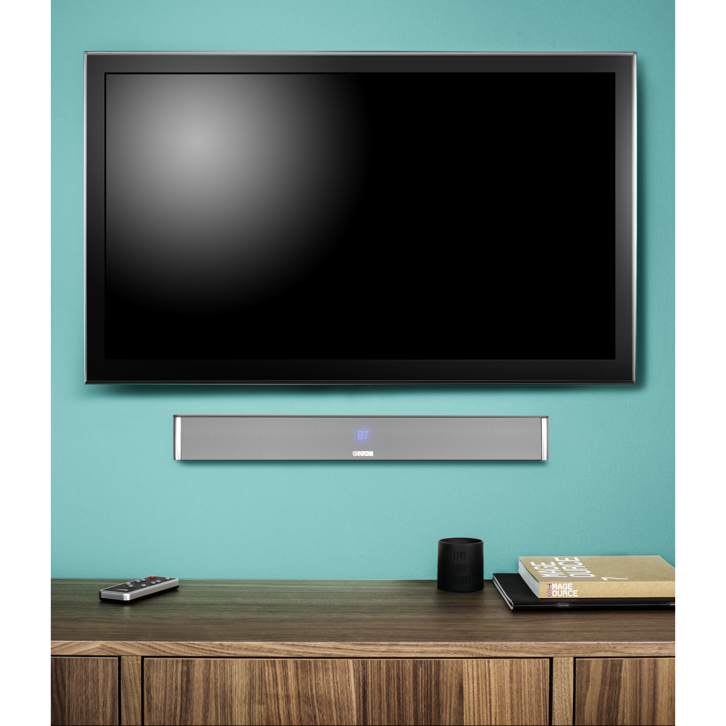 Fernseher an einer türkisfarbenen Wand über einer Soundbar, mit Tisch und Deko.