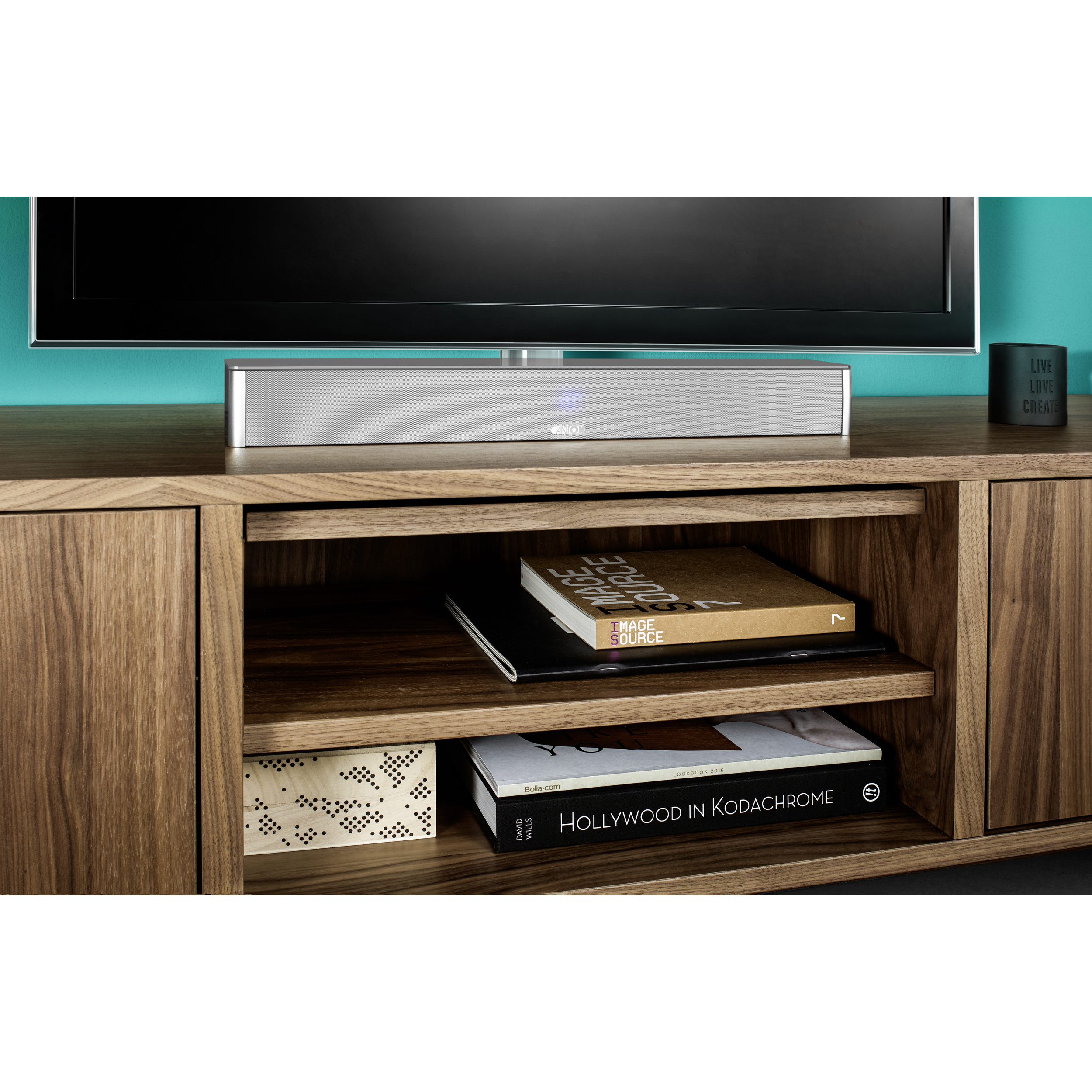 Ein Fernseher steht über einer Soundbar auf einem Holzschrank. Bücher und Dekorationsartikel befinden sich auf den Regalen darunter.