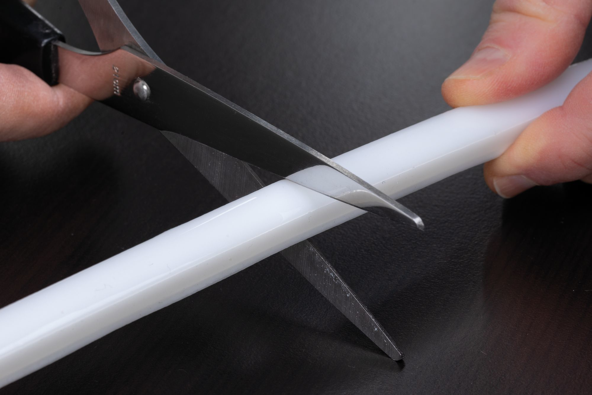 Ciseaux coupant un tube plastique blanc. Mains tenant les ciseaux et le tube.