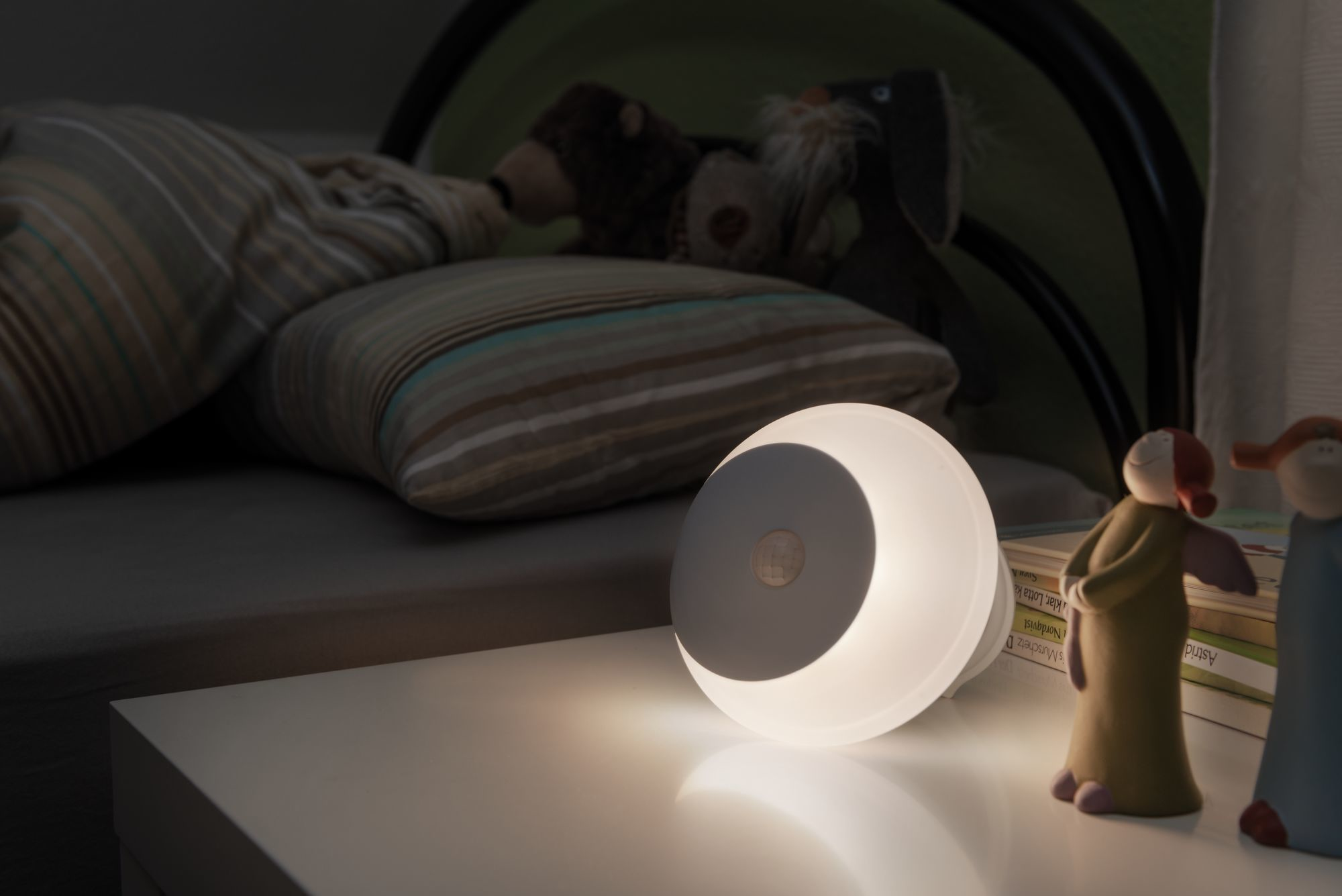 Ein weißes und graues Nachtlicht auf einem Tisch mit einem Bett.