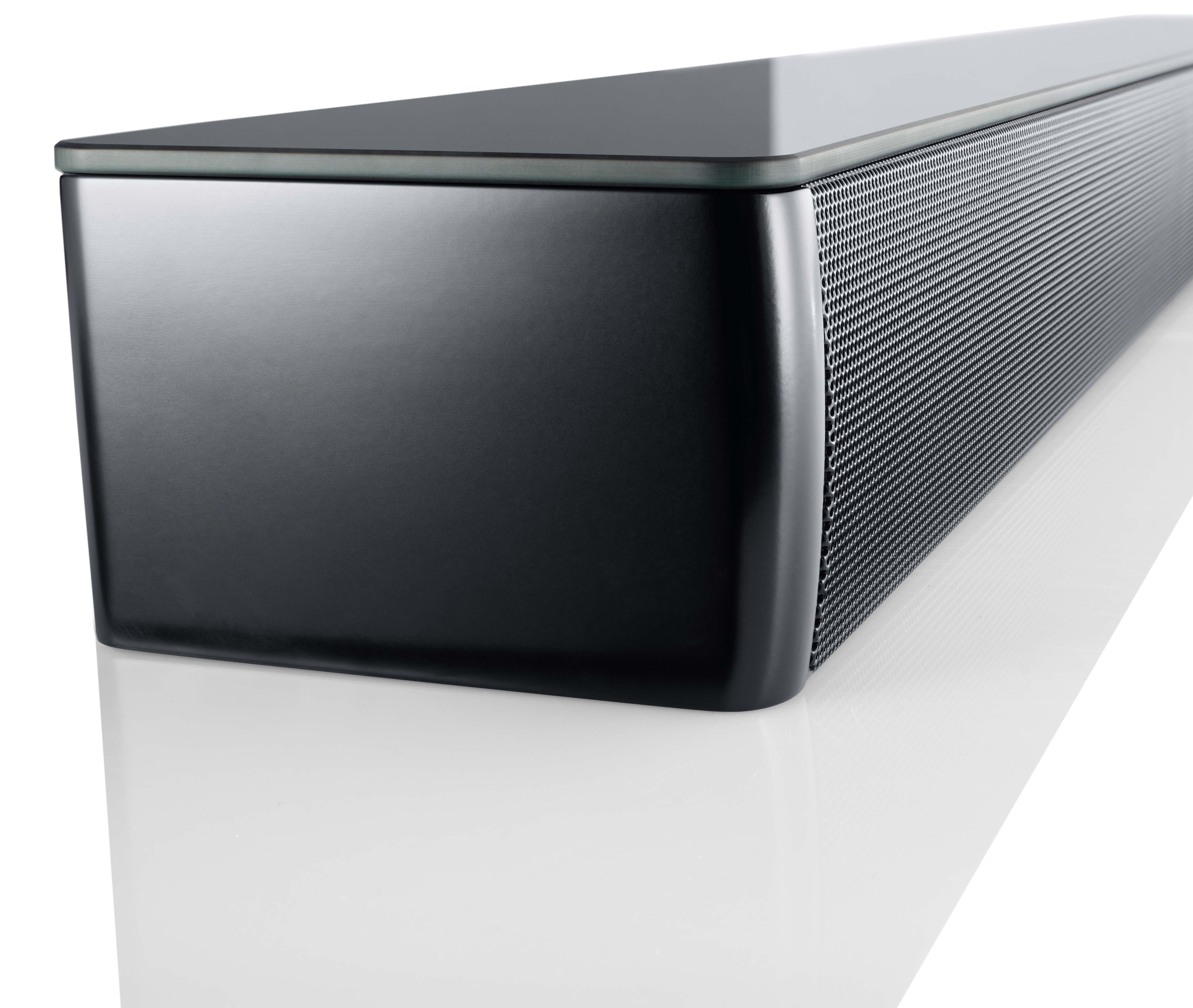 Czarny soundbar z siatkowym przodem, błyszczącą górną powierzchnią i białym odbiciem. Gładkie białe tło.