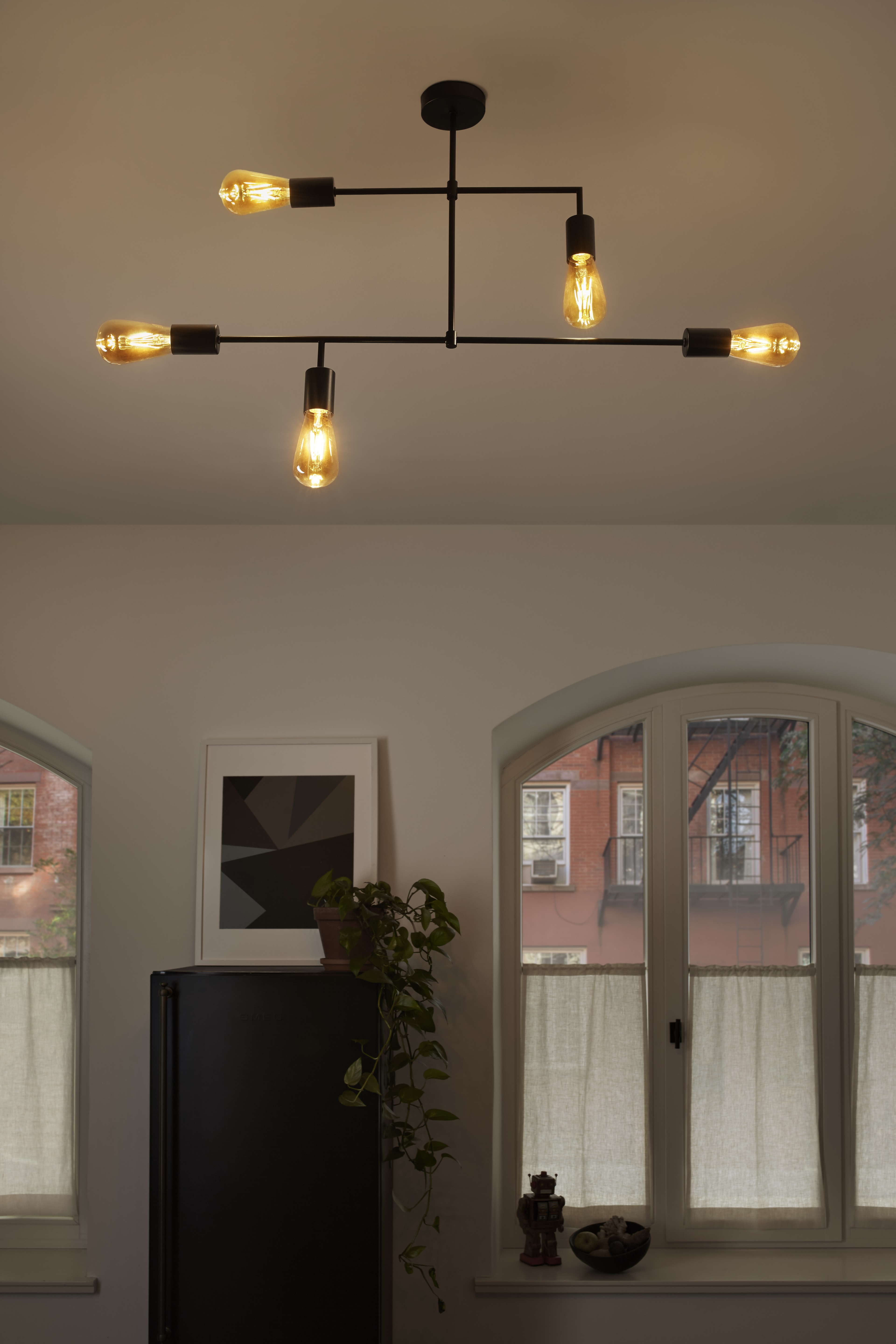 Lampada da soffitto con quattro lampadine Edison, sopra un mobile nero e una finestra con vista.