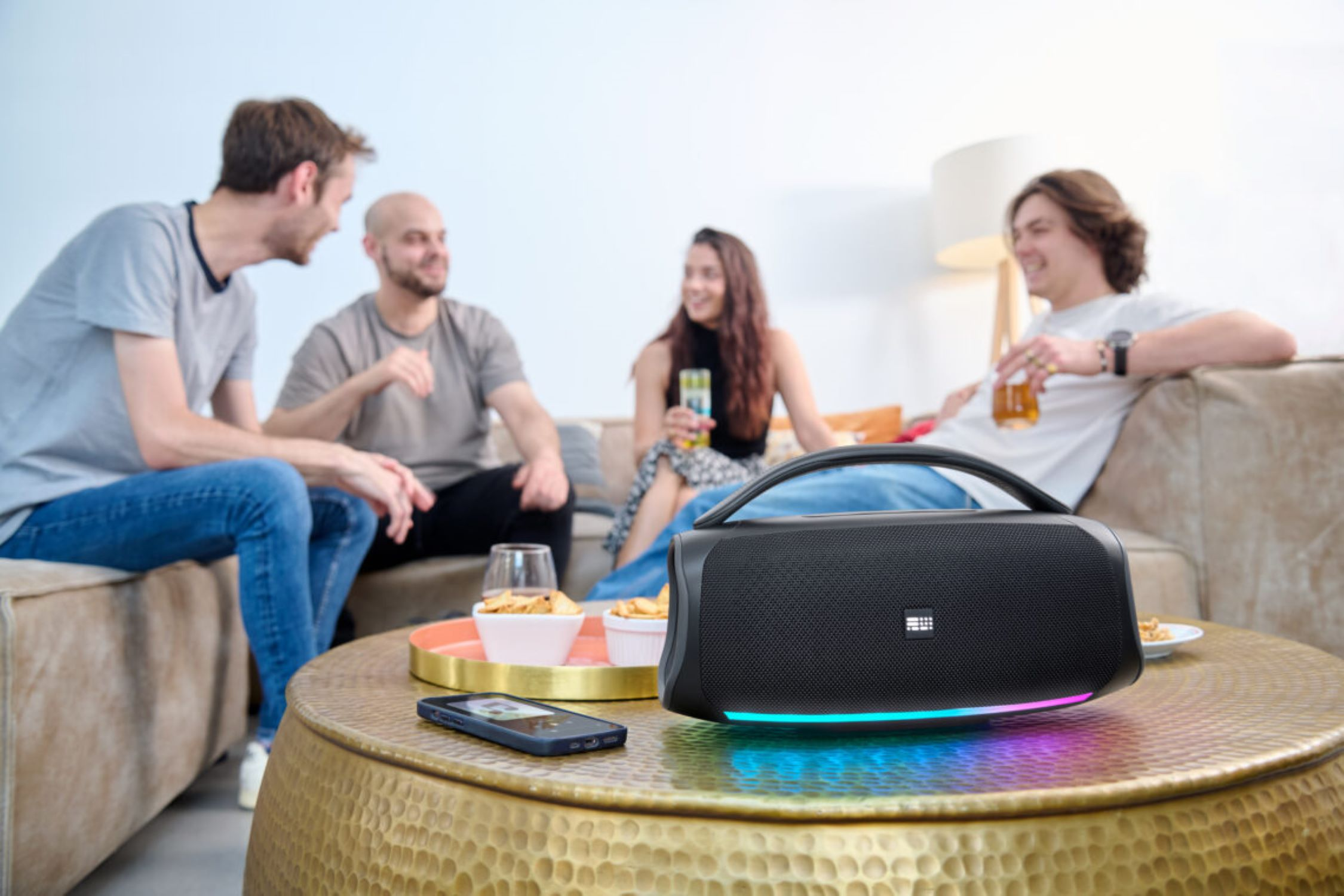 Un altoparlante nero con persone sullo sfondo. C'è un telefono e degli snack sul tavolo.