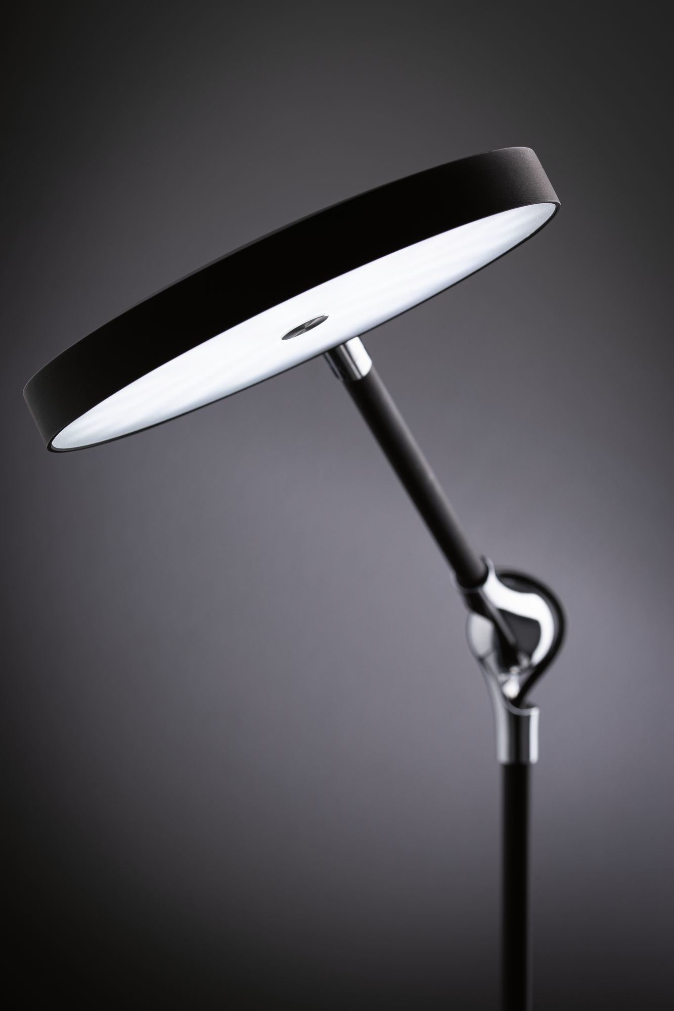 Eine schwarze moderne Schreibtischlampe mit rundem Licht auf dunklem Hintergrund.