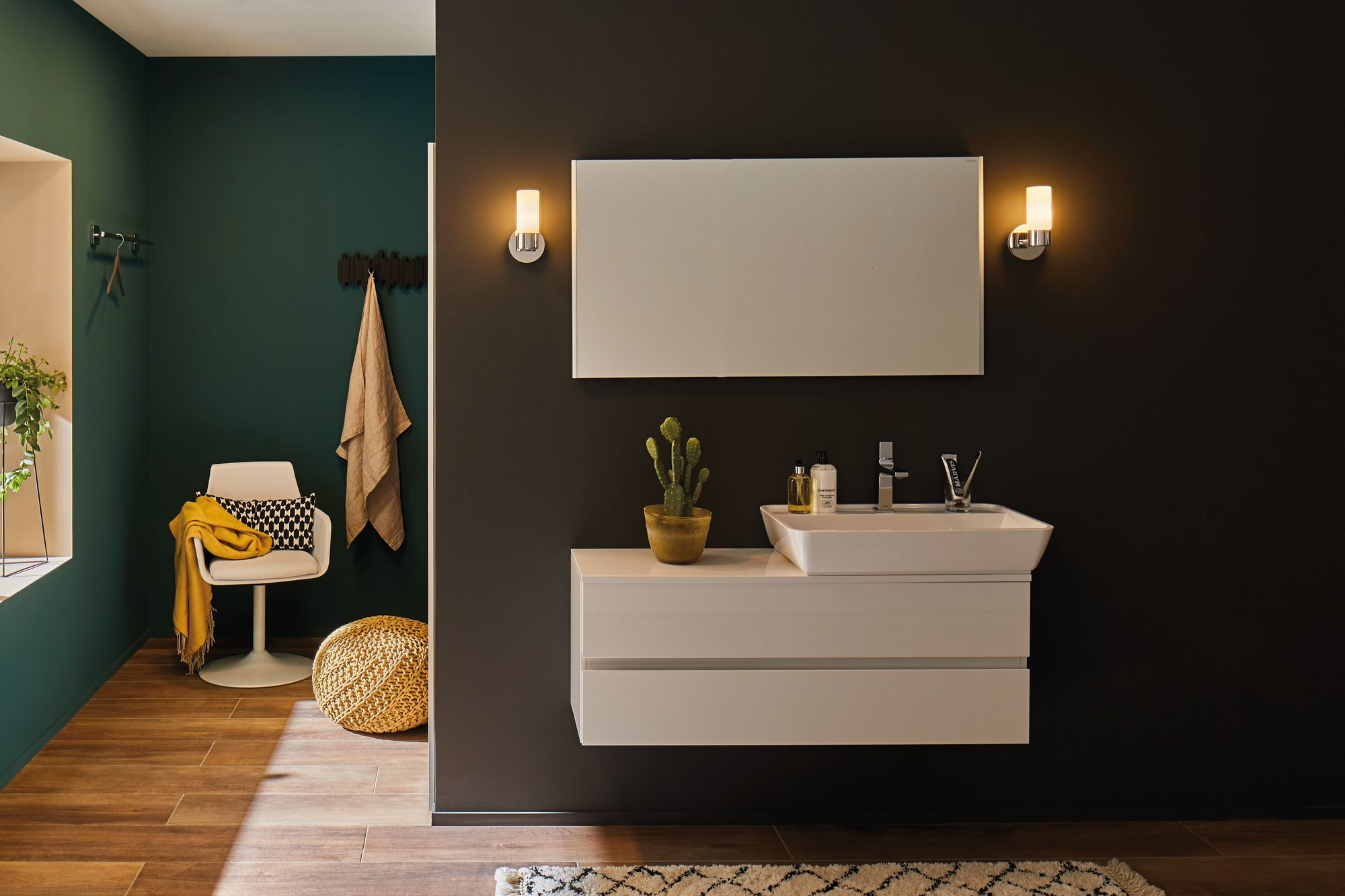 Salle de bain avec lavabo blanc, miroir et cactus, murs noirs et verts.