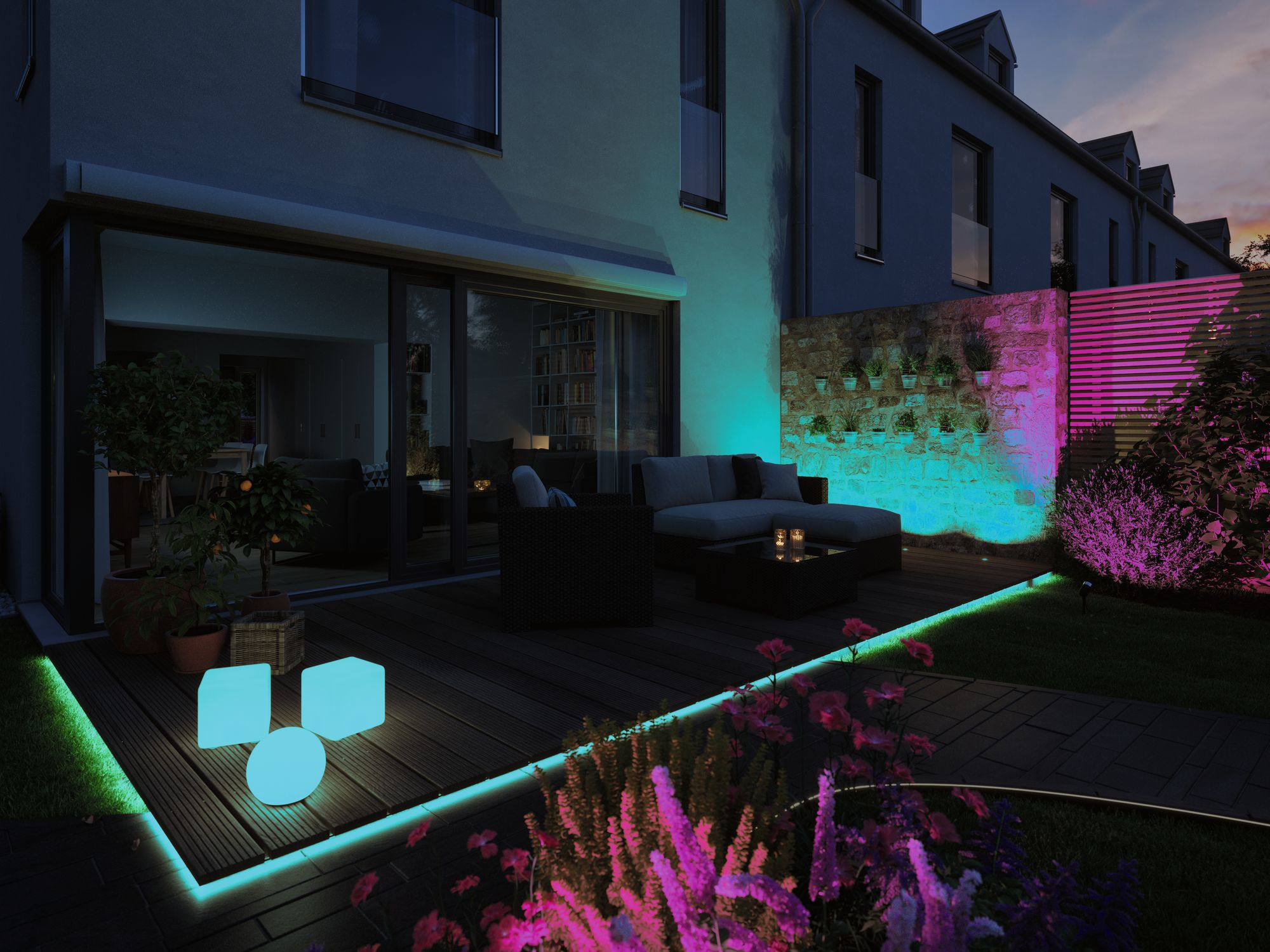 Scena na zewnątrz o zmierzchu z tarasem, światłami i domem. Światła są kolorowe.