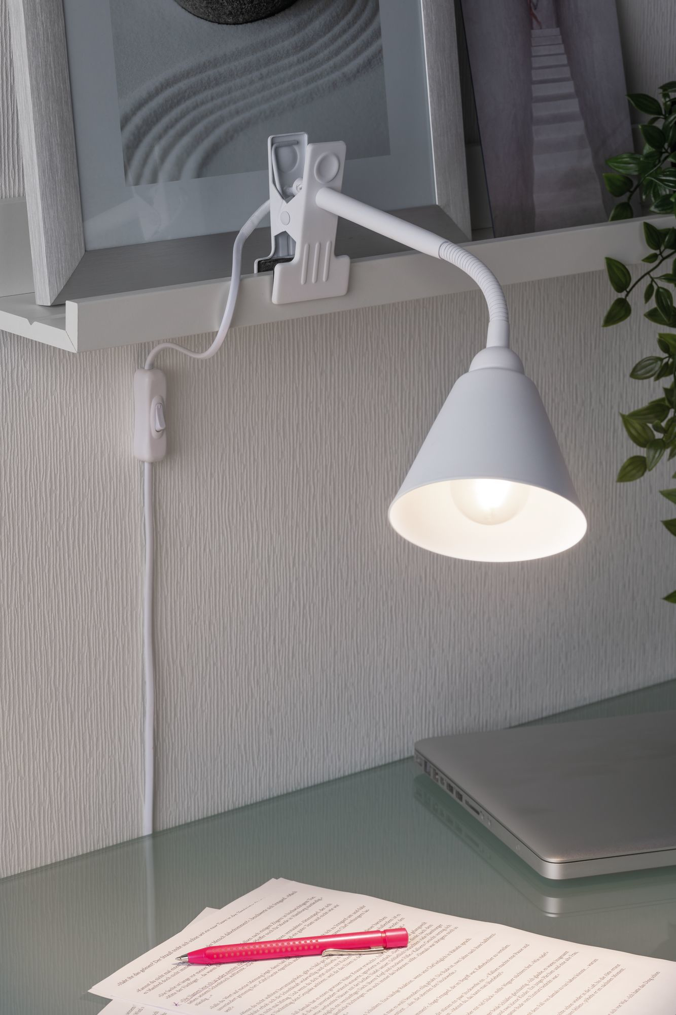 Eine weiße Schreibtischlampe beleuchtet einen Schreibtisch mit Bilderrahmen und Papieren.