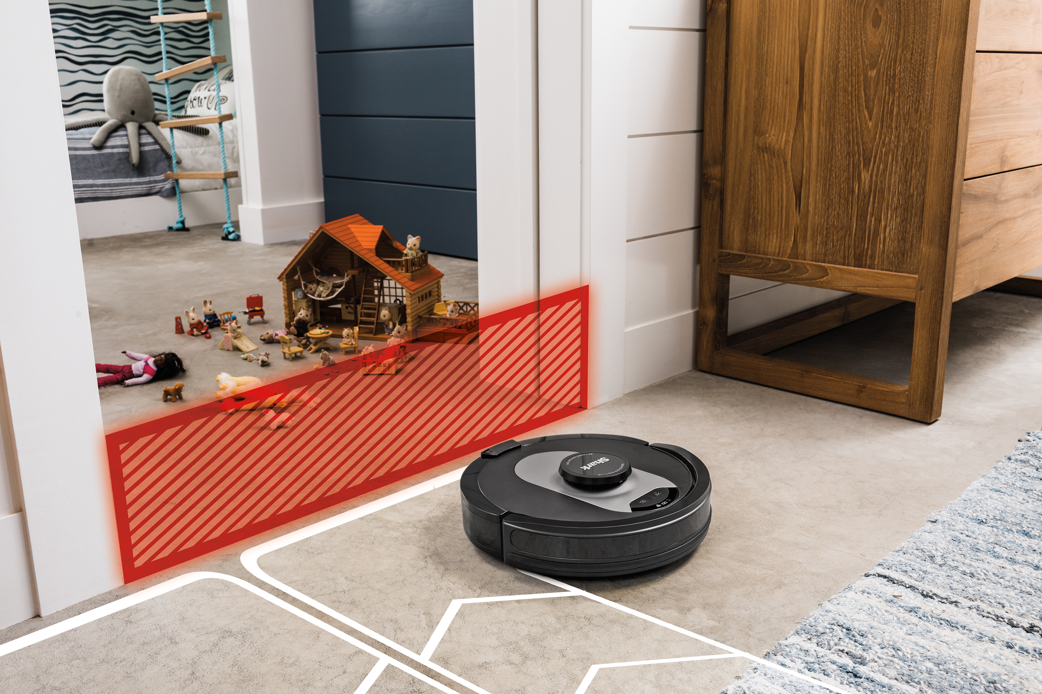 Czarny odkurzacz robot w pokoju z zabawkami, drzwiami i białymi ścianami.