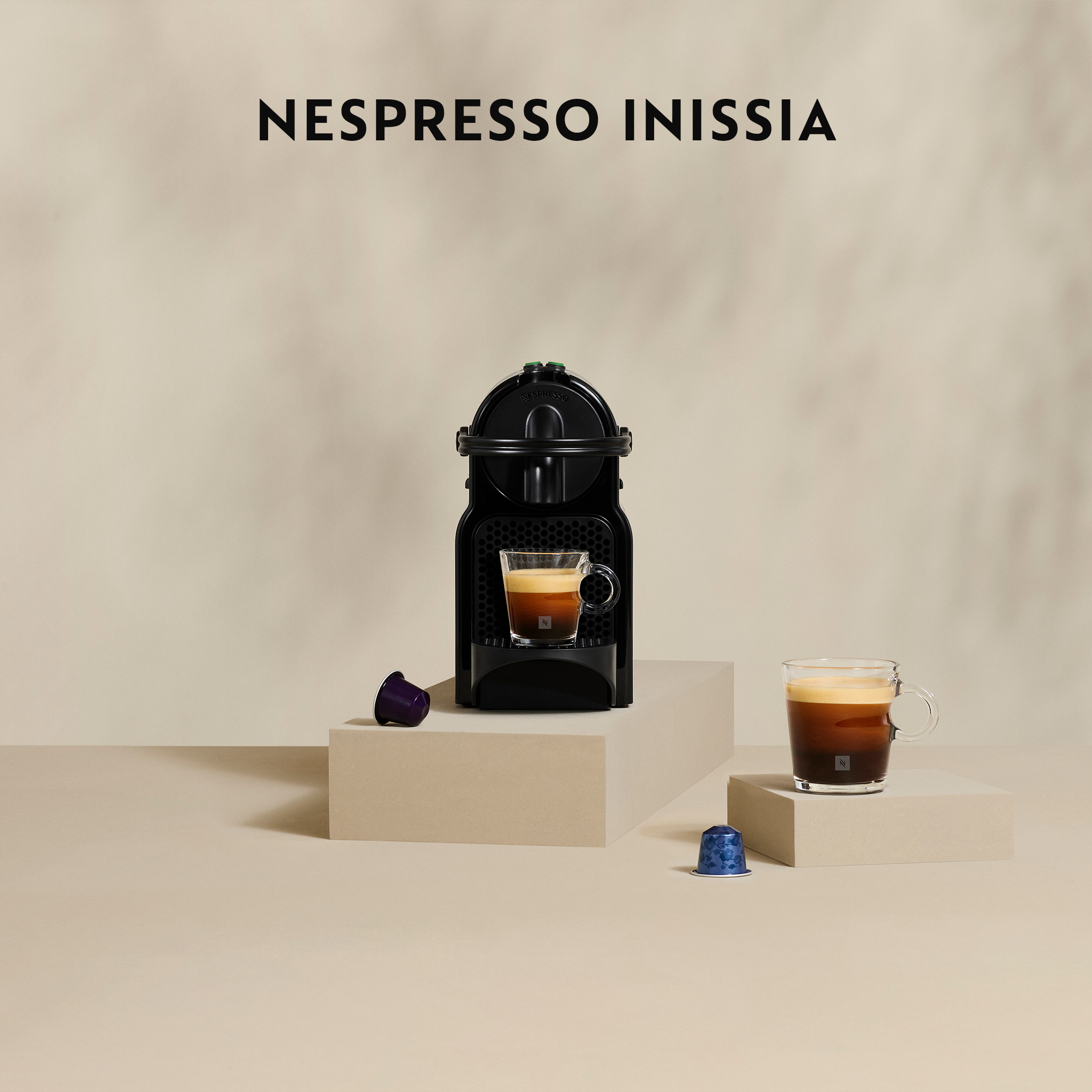 Eine Nespresso Inissia Kaffeemaschine mit zwei Tassen Kaffee und zwei Kaffeekapseln.