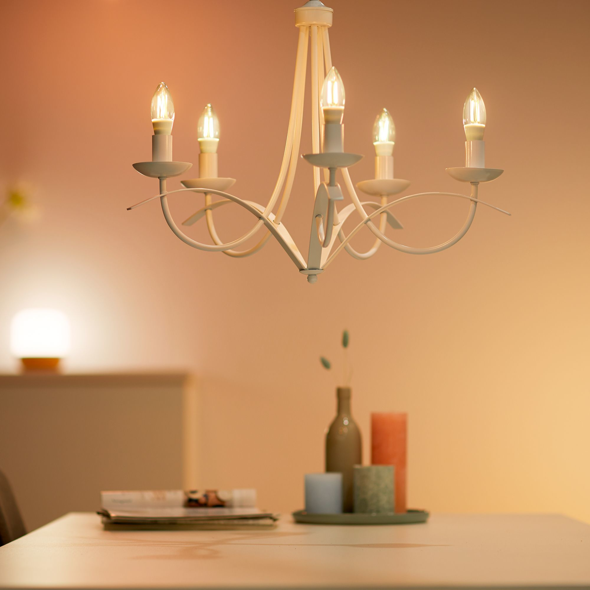 Żyrandol z zapalonymi świecami. Tło przedstawia stół i przedmioty na nim.