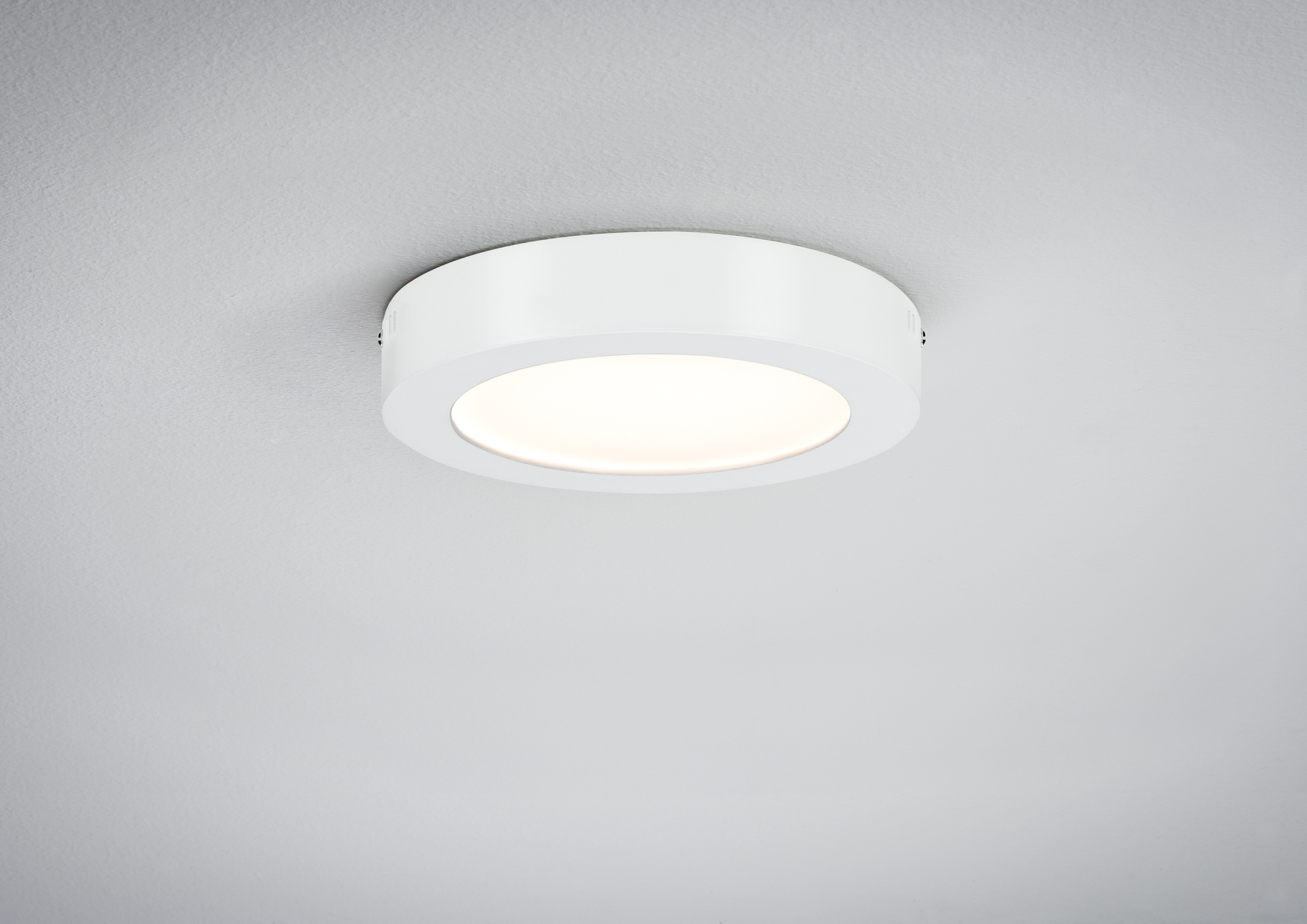 Eine weiße, runde Deckenleuchte mit einem vertieften Licht. Es ist an einer weißen Decke.