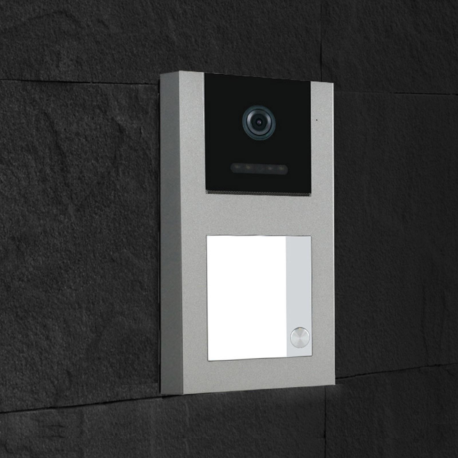 Silbernes Intercom-System mit Kamera und Licht, an einer schwarzen Steinmauer montiert.