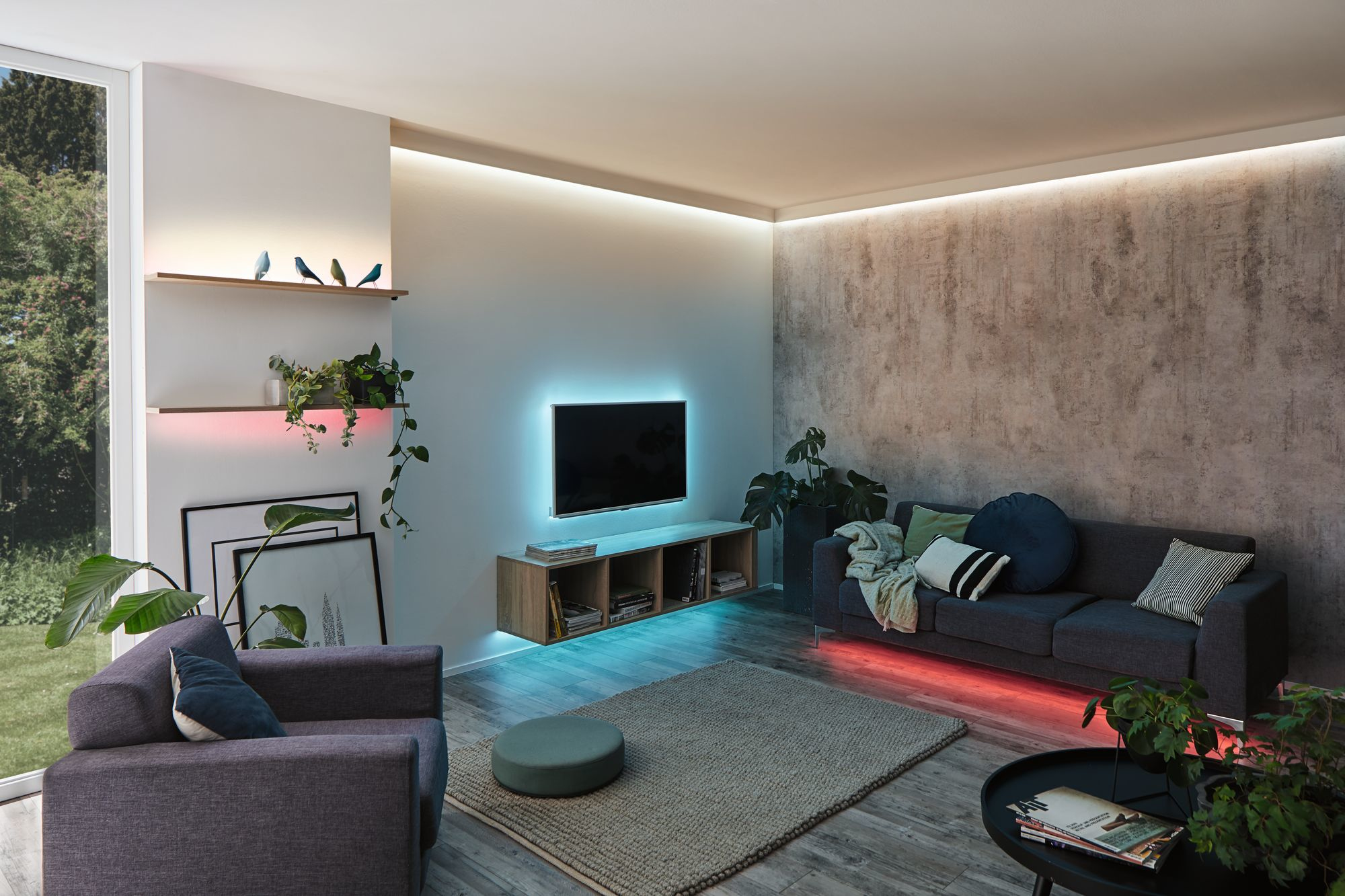 Wohnzimmer mit farbenfroher LED-Beleuchtung um TV, Sofa und Regale. Modernes und stilvolles Design.