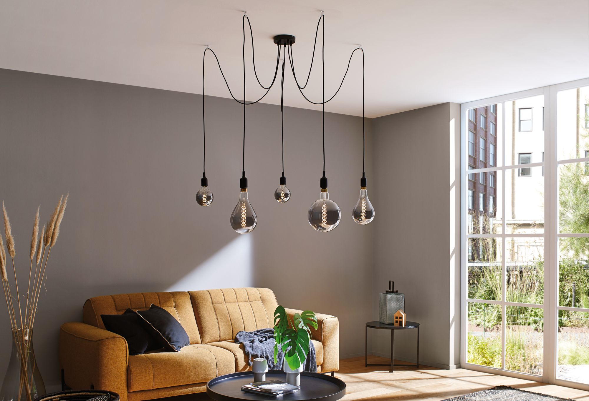 Scène de salon avec un canapé moutarde, des objets décoratifs et un luminaire suspendu.