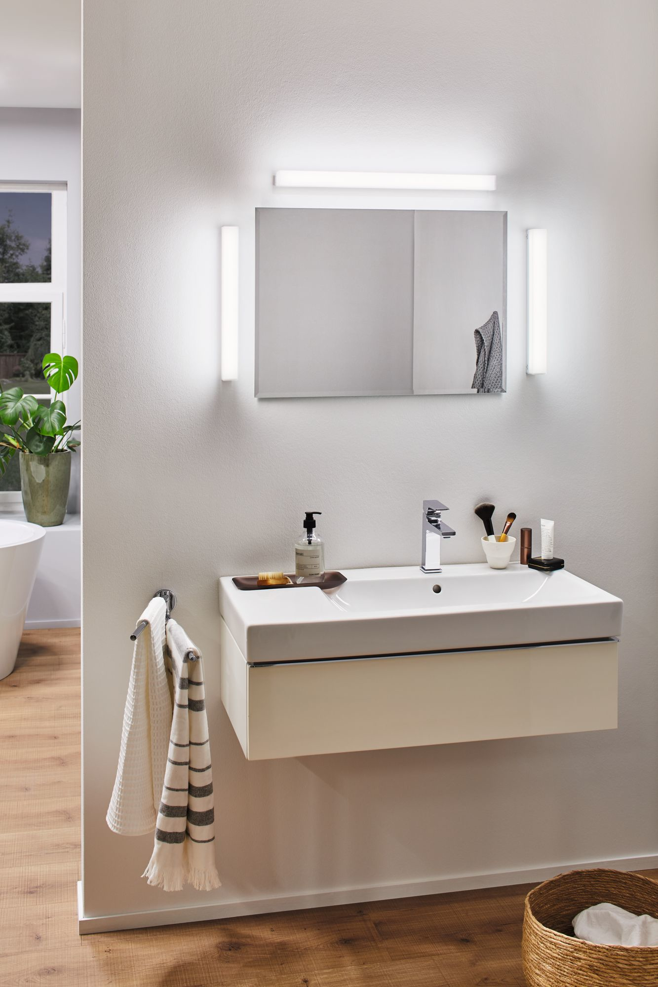 Biała umywalka z kranem, lustrem i światłami. Ręcznik wisi z boku.