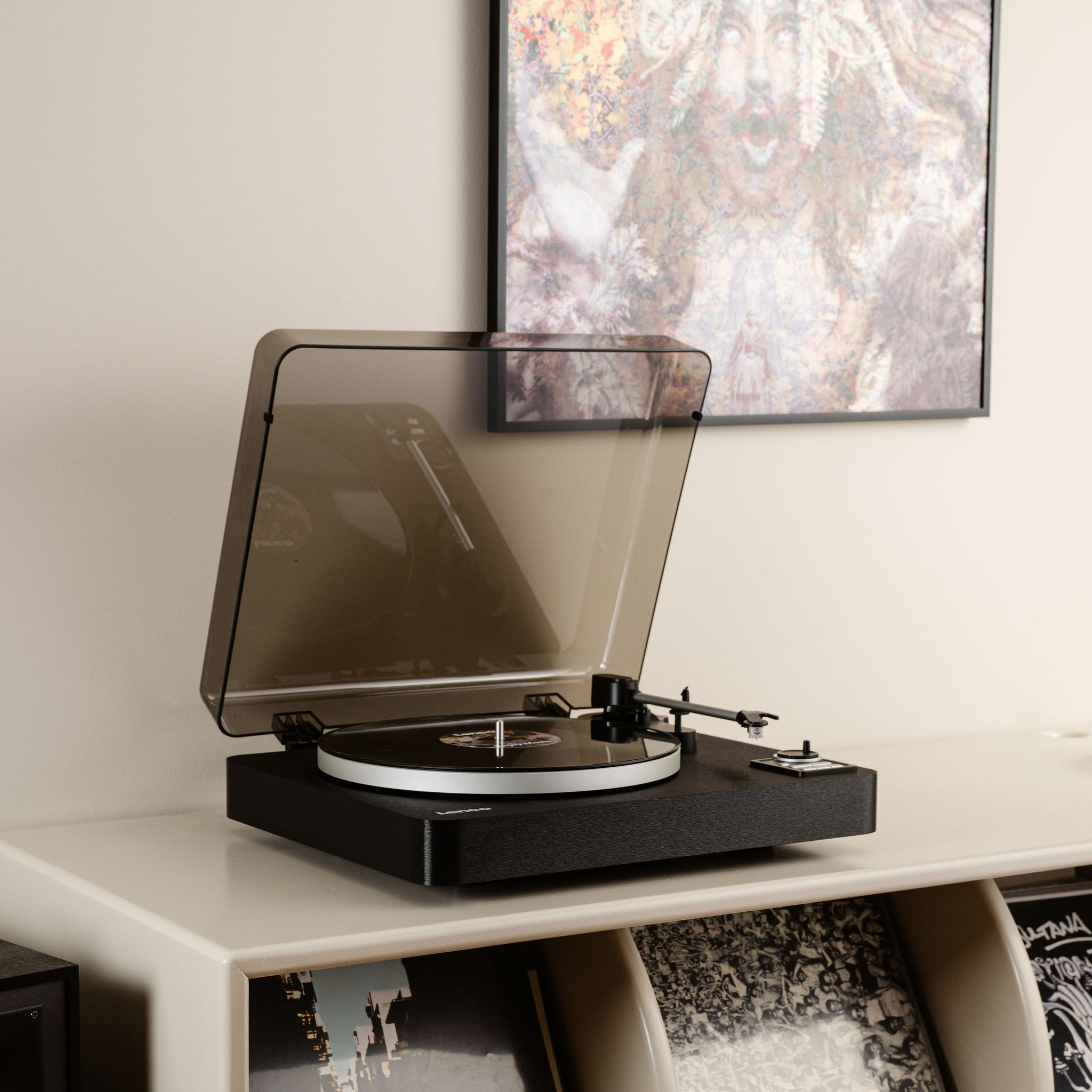 Czarny gramofon na białej szafce z płytami i obrazem w tle.