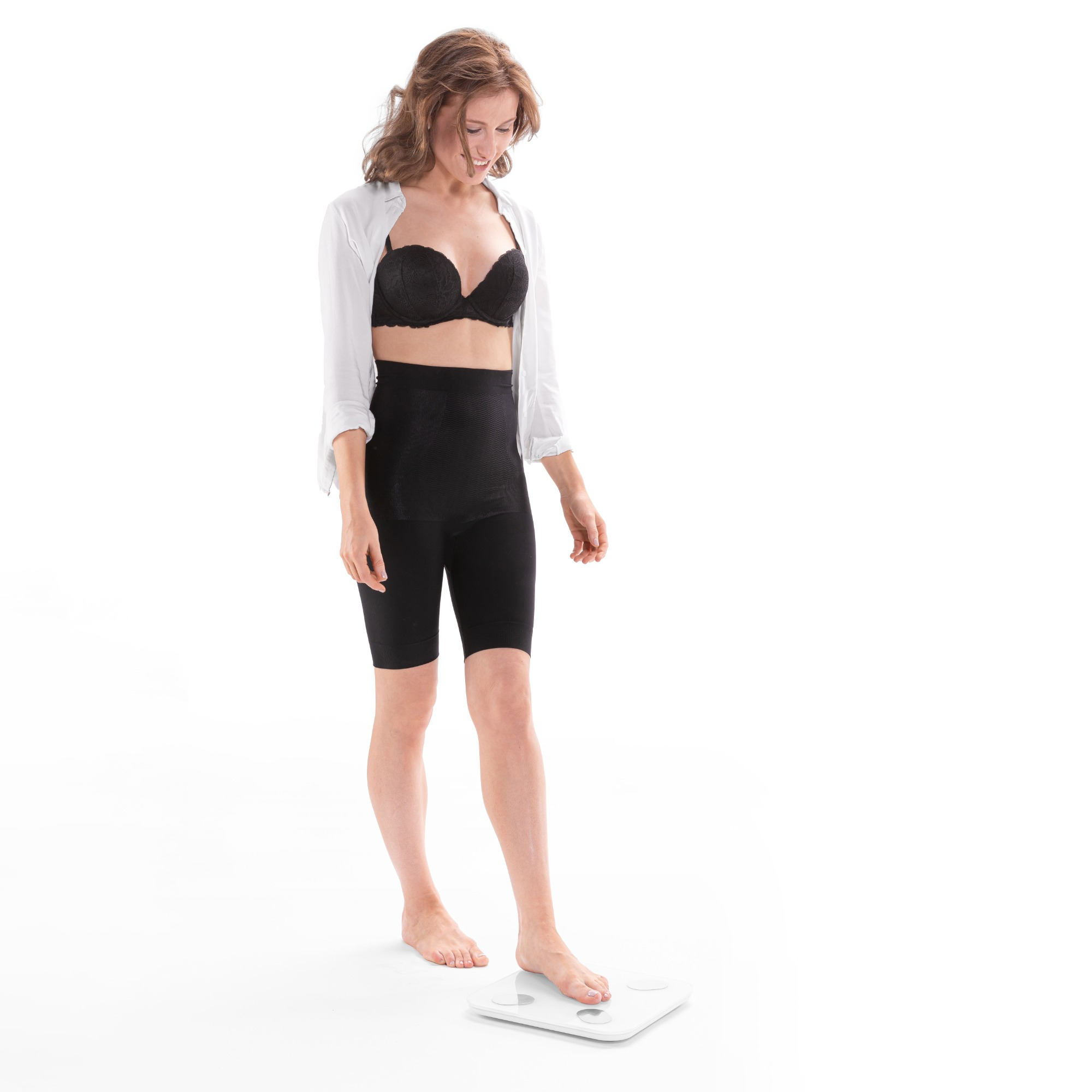 Eine Frau in BH und Shorts steht auf einer Waage und lächelt.