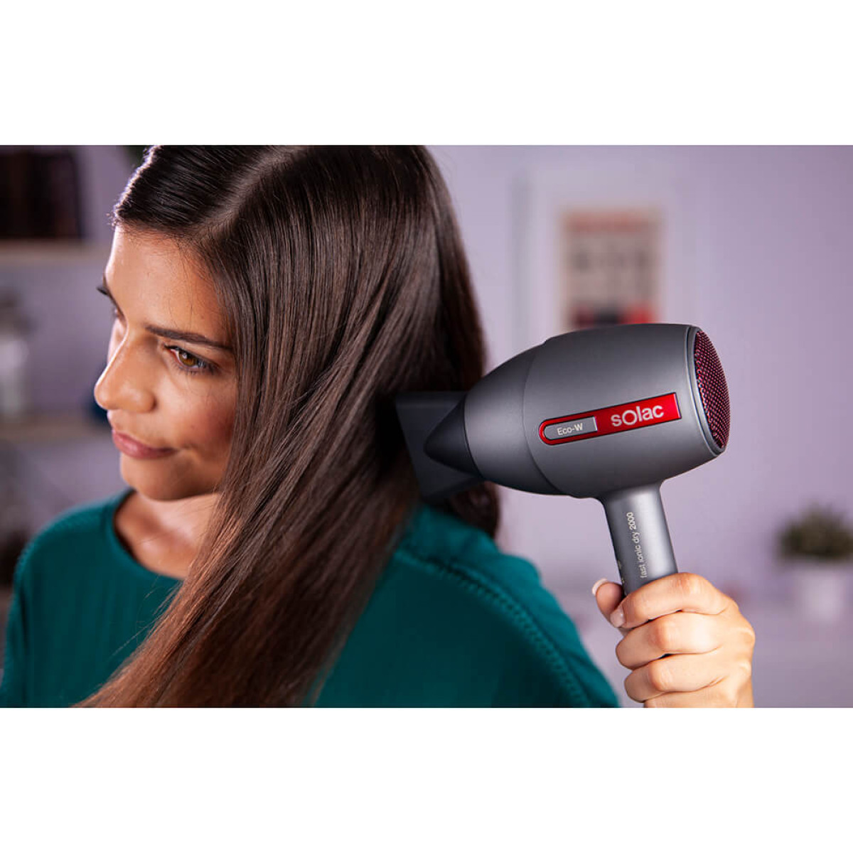 Mujer secándose el pelo con un secador de pelo gris. Tiene una rejilla roja y la marca Solac.