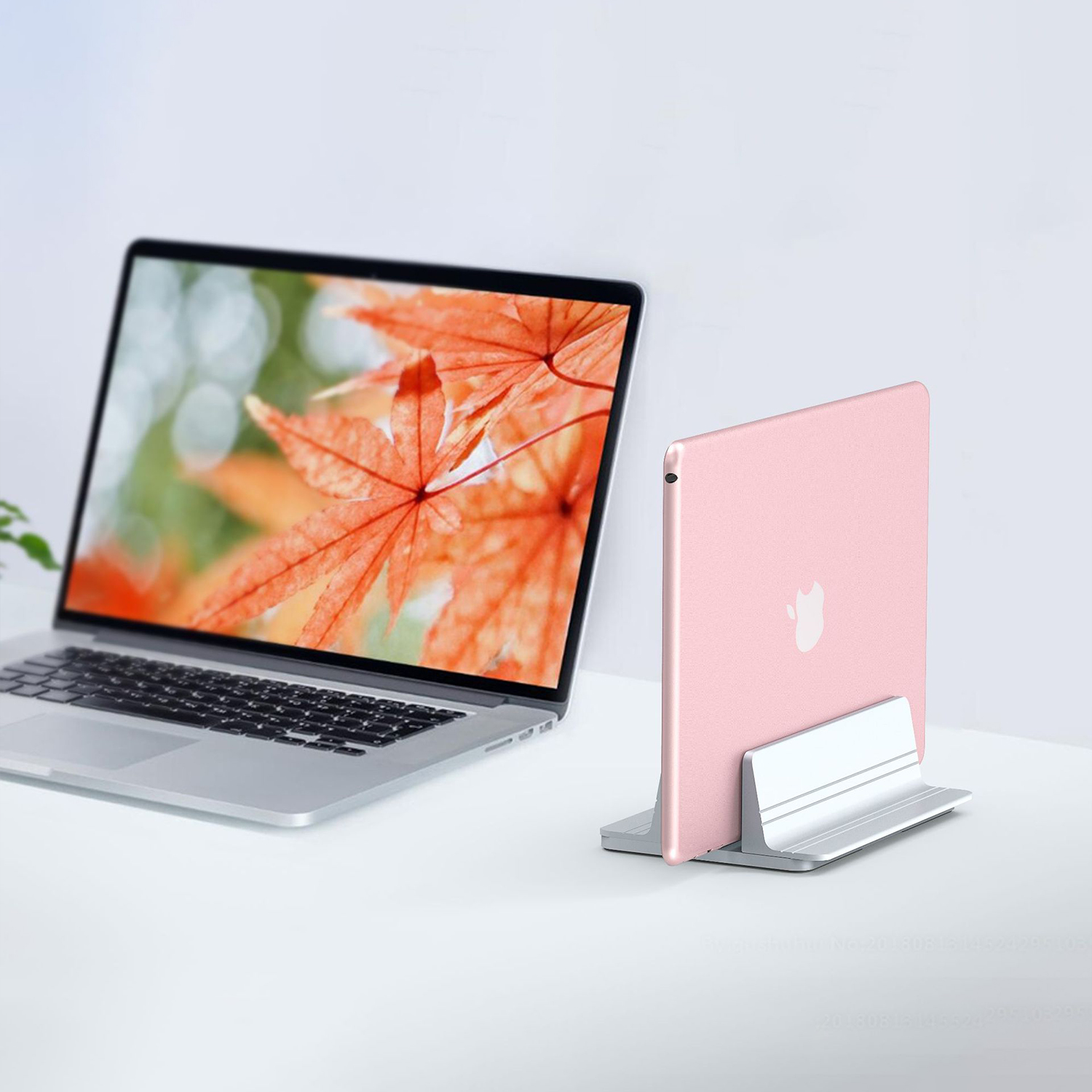 Ein Laptop und ein rosa Tablet in einem Ständer auf weißer Oberfläche. Ahornblatt auf dem Bildschirm.