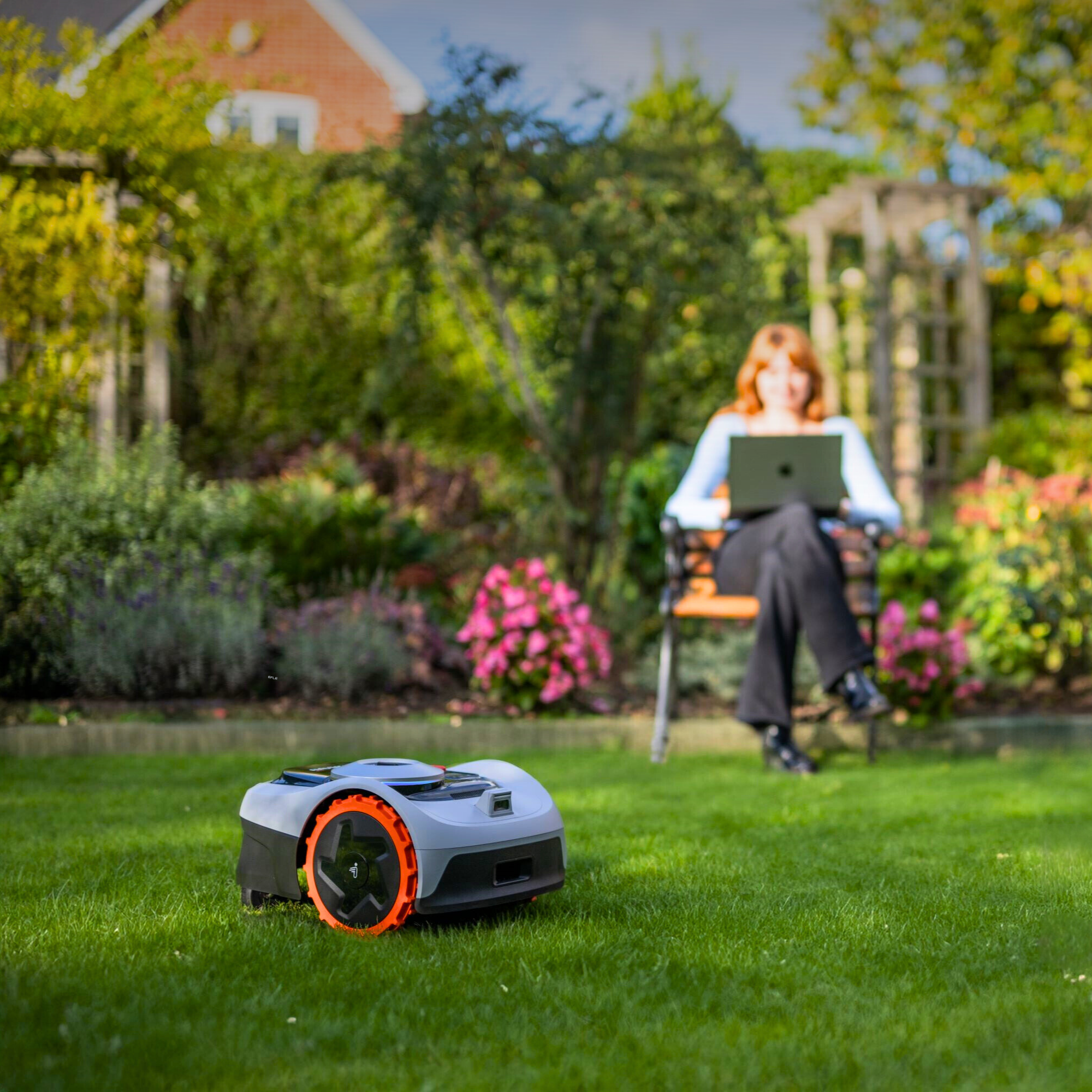 Robot koszący i kobieta korzystająca z laptopa w ogrodzie.