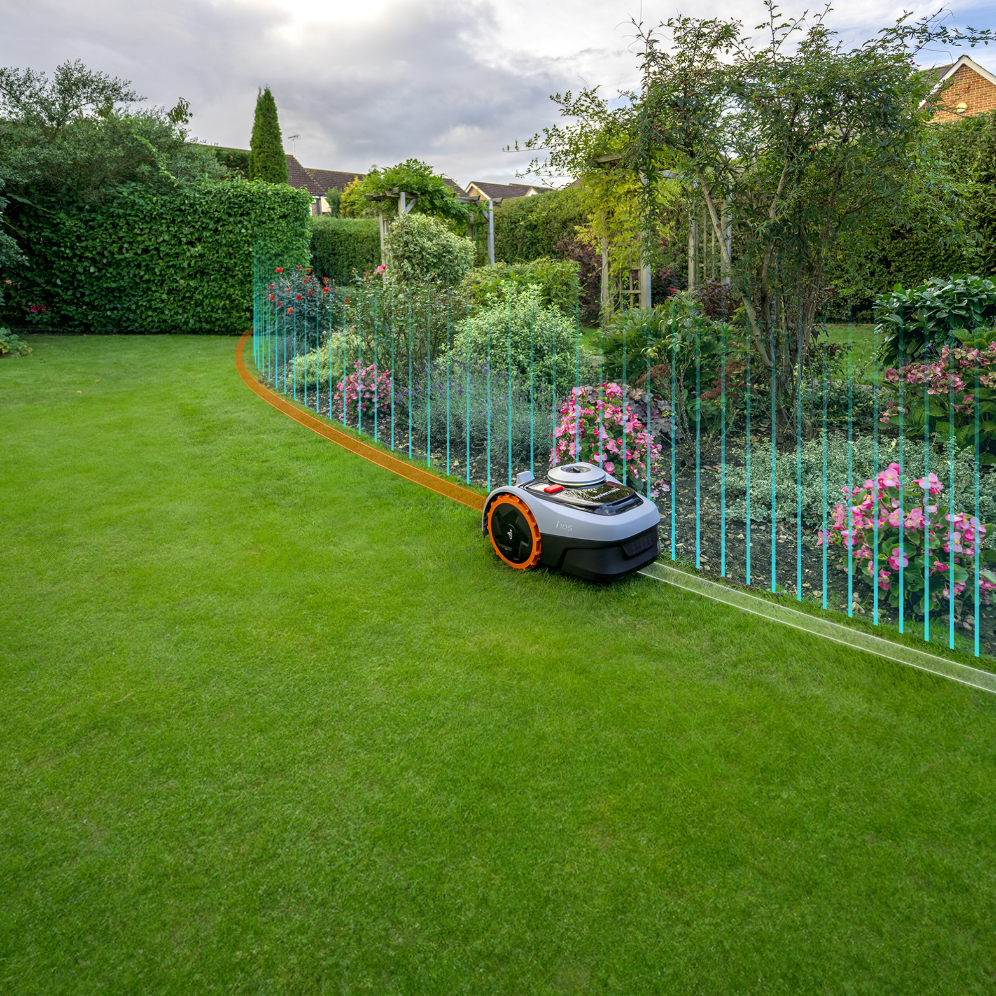 Robotyczna kosiarka na trawie, w pobliżu rabaty kwiatowej z przewodem obwodowym i zachmurzonym niebem.