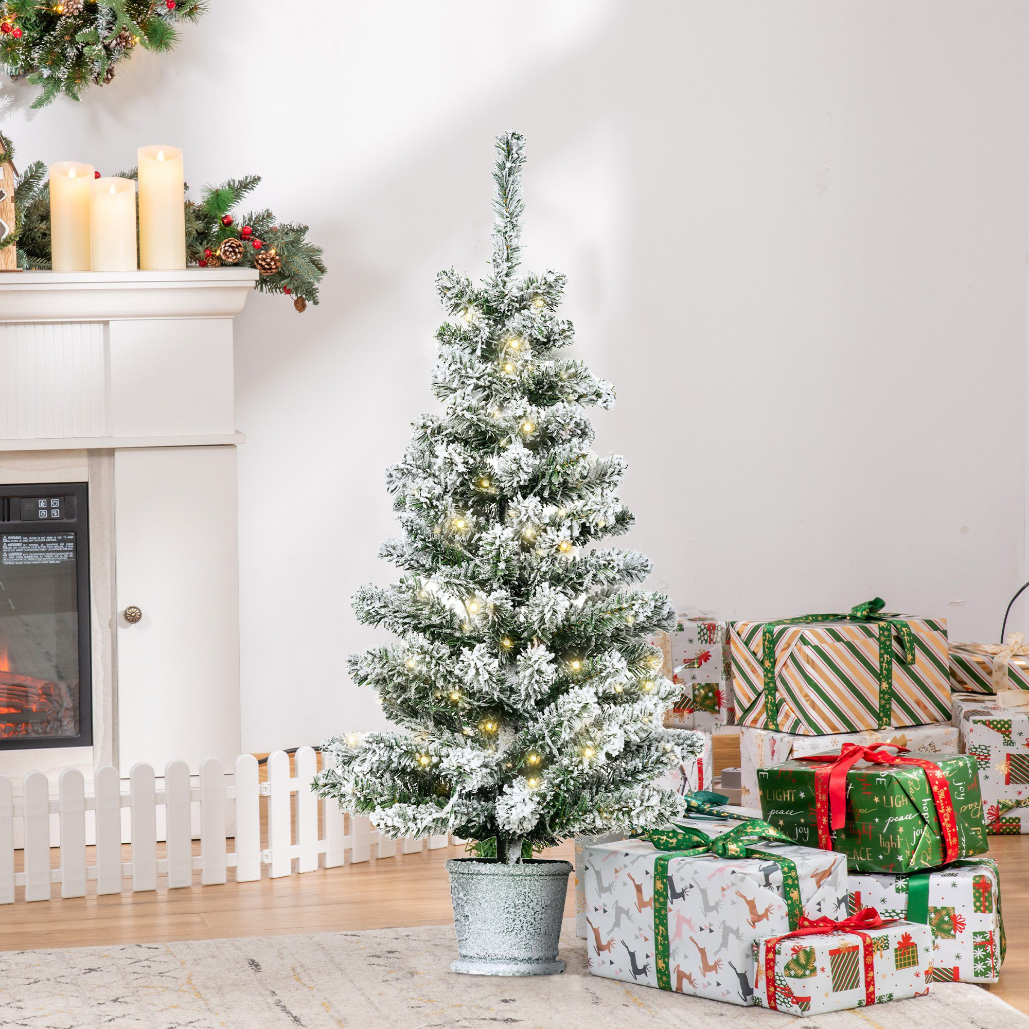 Un árbol de Navidad con decoraciones blancas, una maceta y cajas de regalo. Una chimenea al fondo.